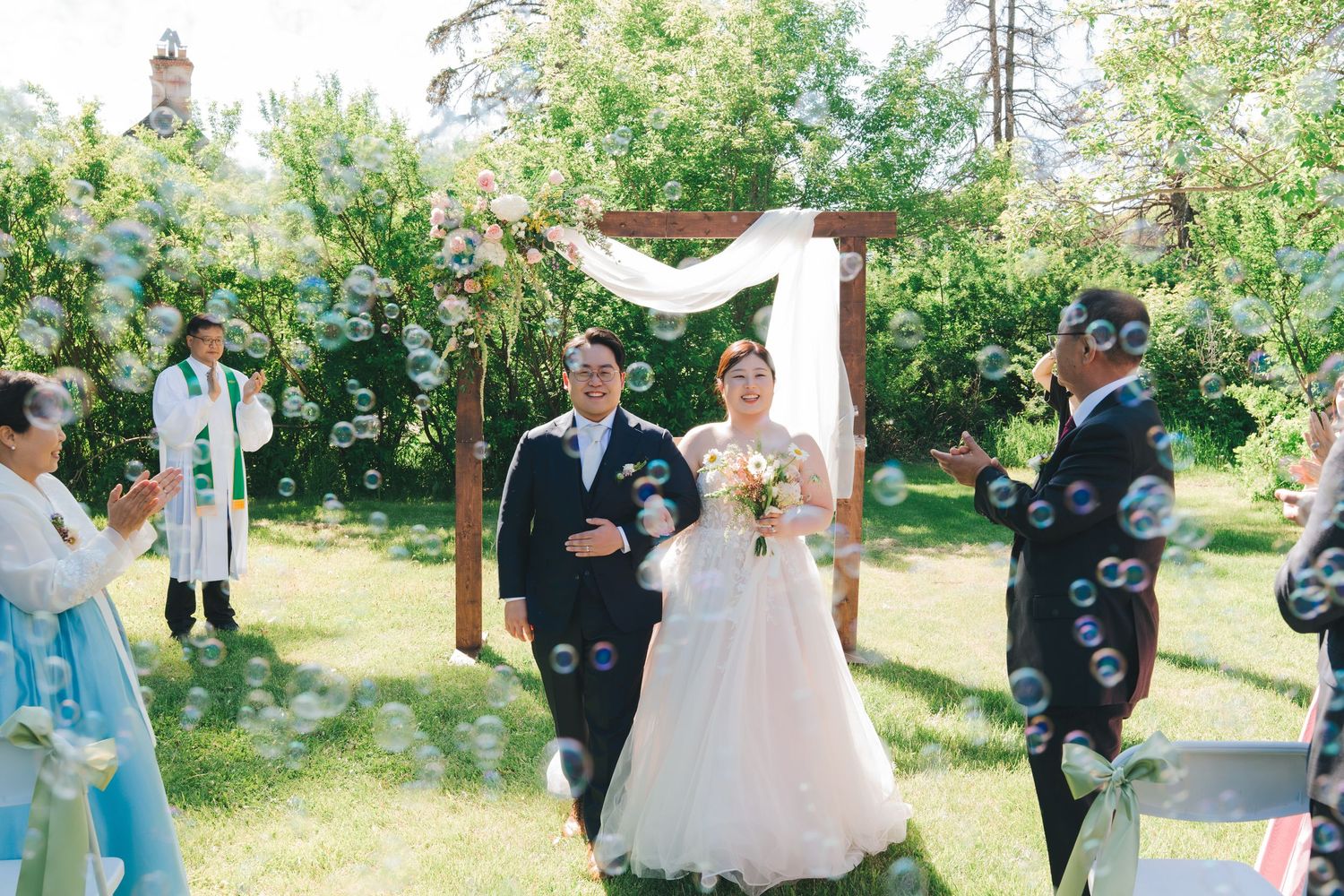 Bride and groom walking through bubbles after outdoor wedding ceremony.