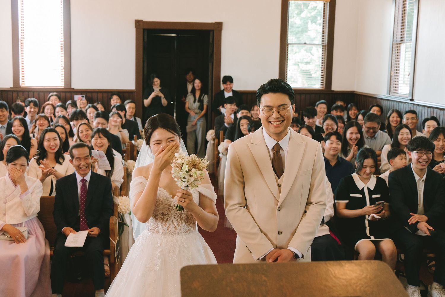 Bride and groom stand together at altar as wedding guests smile and celebrate in church pews.