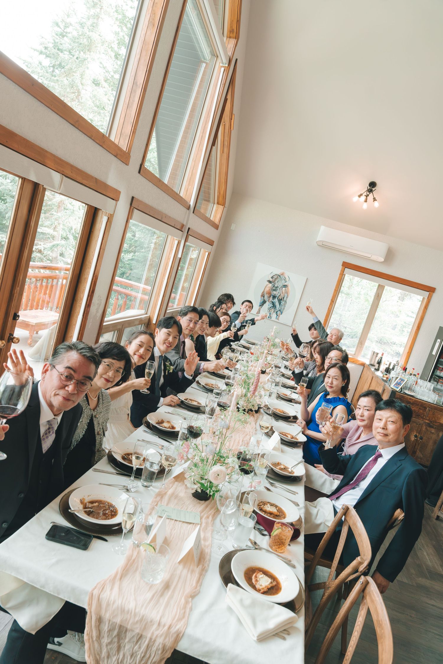 Wedding guests celebrating at long decorated reception table in rustic venue.