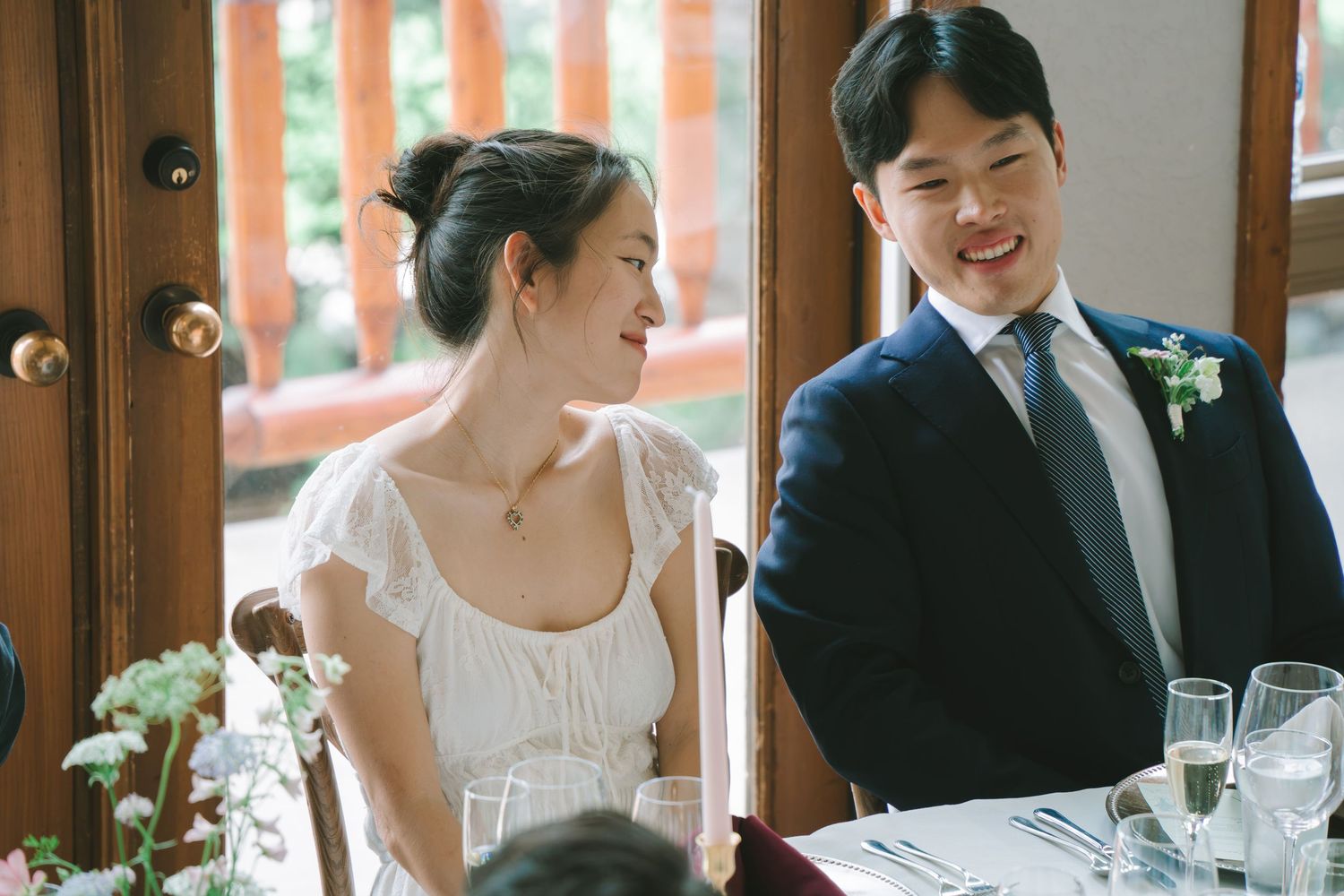 Smiling bride and groom seated together at wedding reception table.