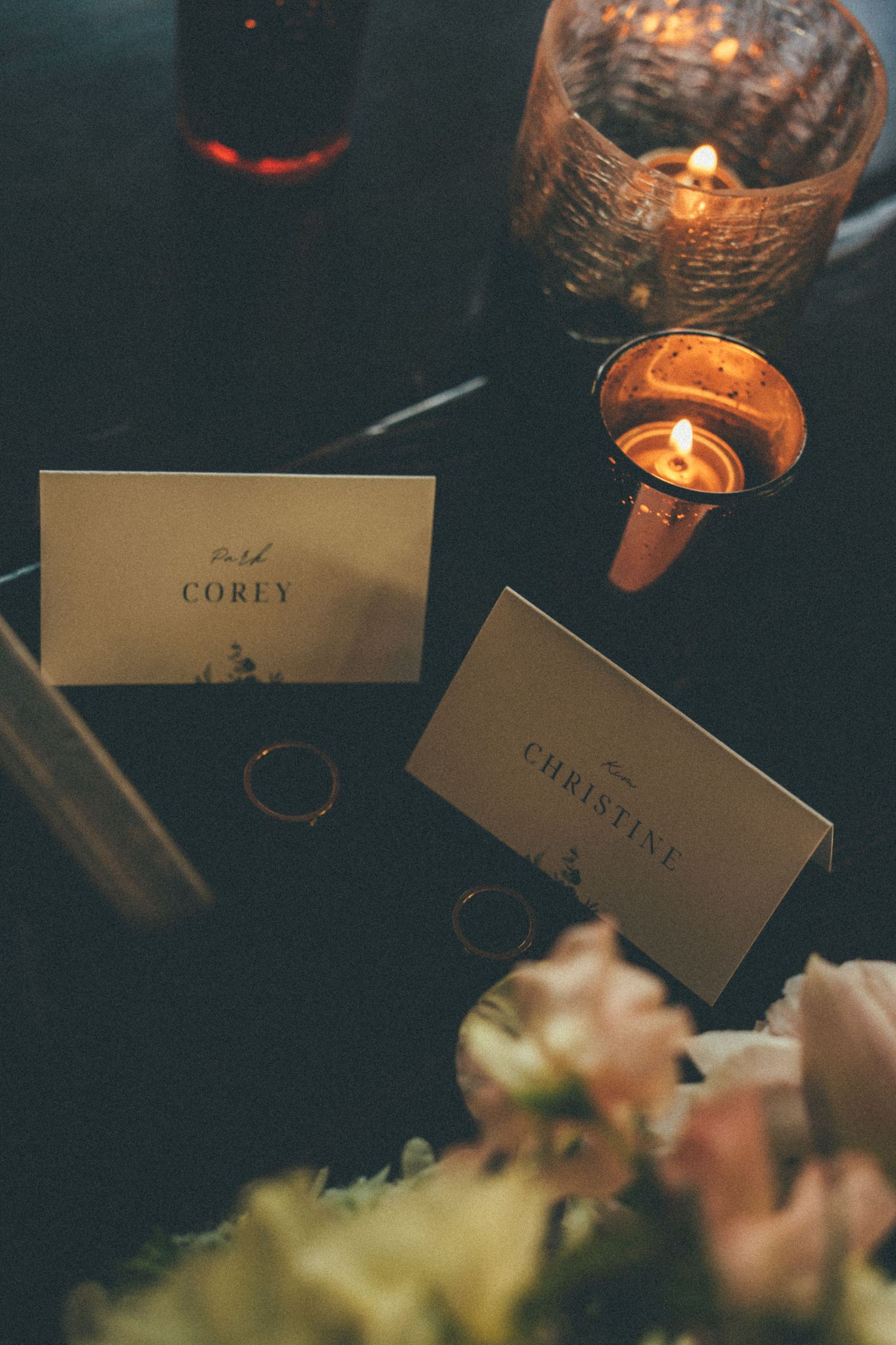 Wedding place cards for Corey and Christine with gold rings and candles on dark table.