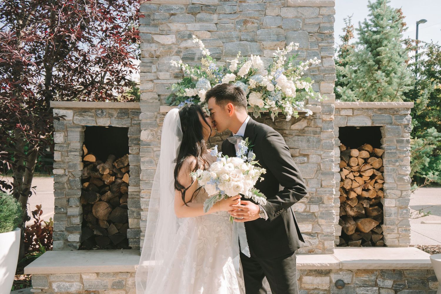 Bride and groom share a romantic kiss in front of a stone fireplace with white floral arch.