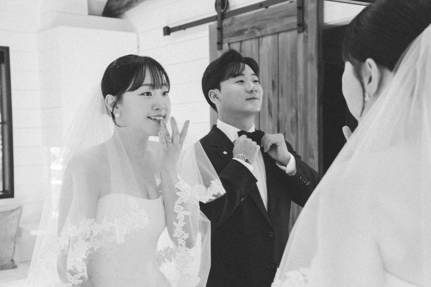 Asian bride and groom share a joyful moment indoors in black and white wedding photo.