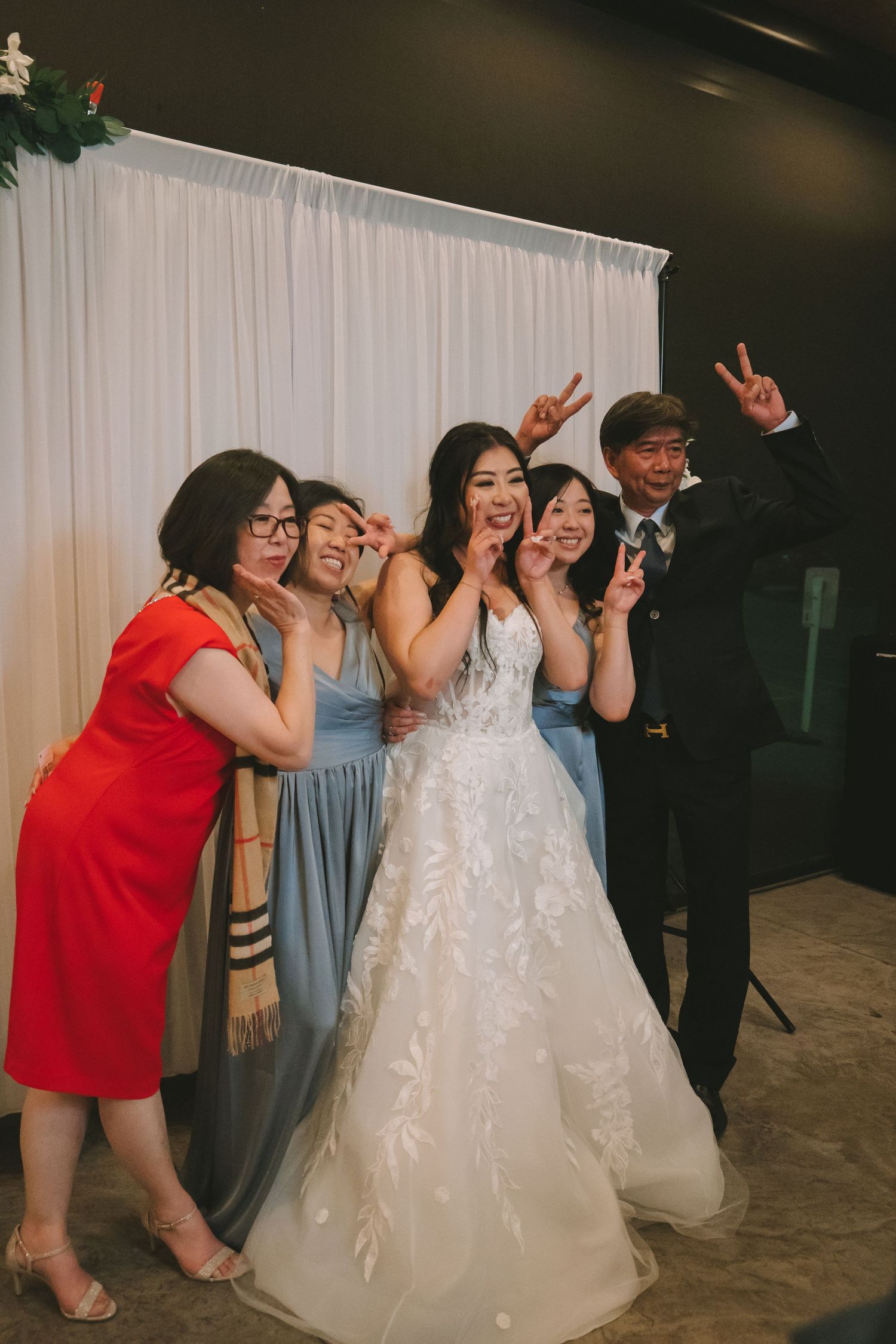 Bride posing with bridesmaids and family making peace signs at wedding reception.