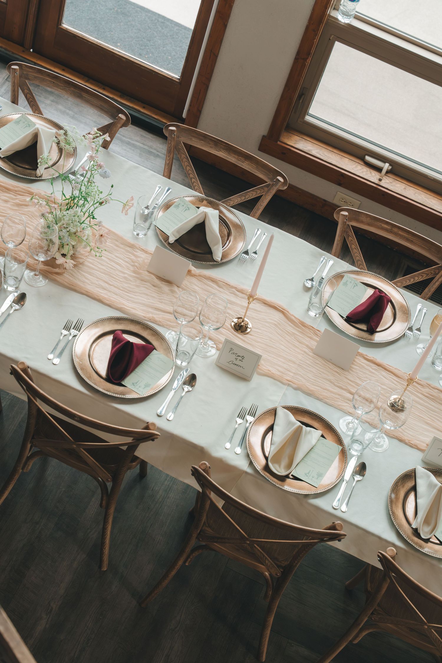 Elegant wedding reception table set with gold chargers and burgundy napkins.