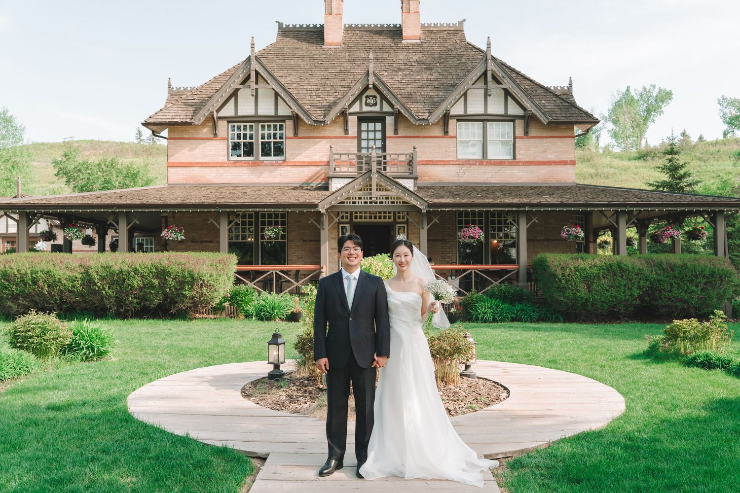 Asian bride and groom pose together in front of elegant brick wedding venue exterior.