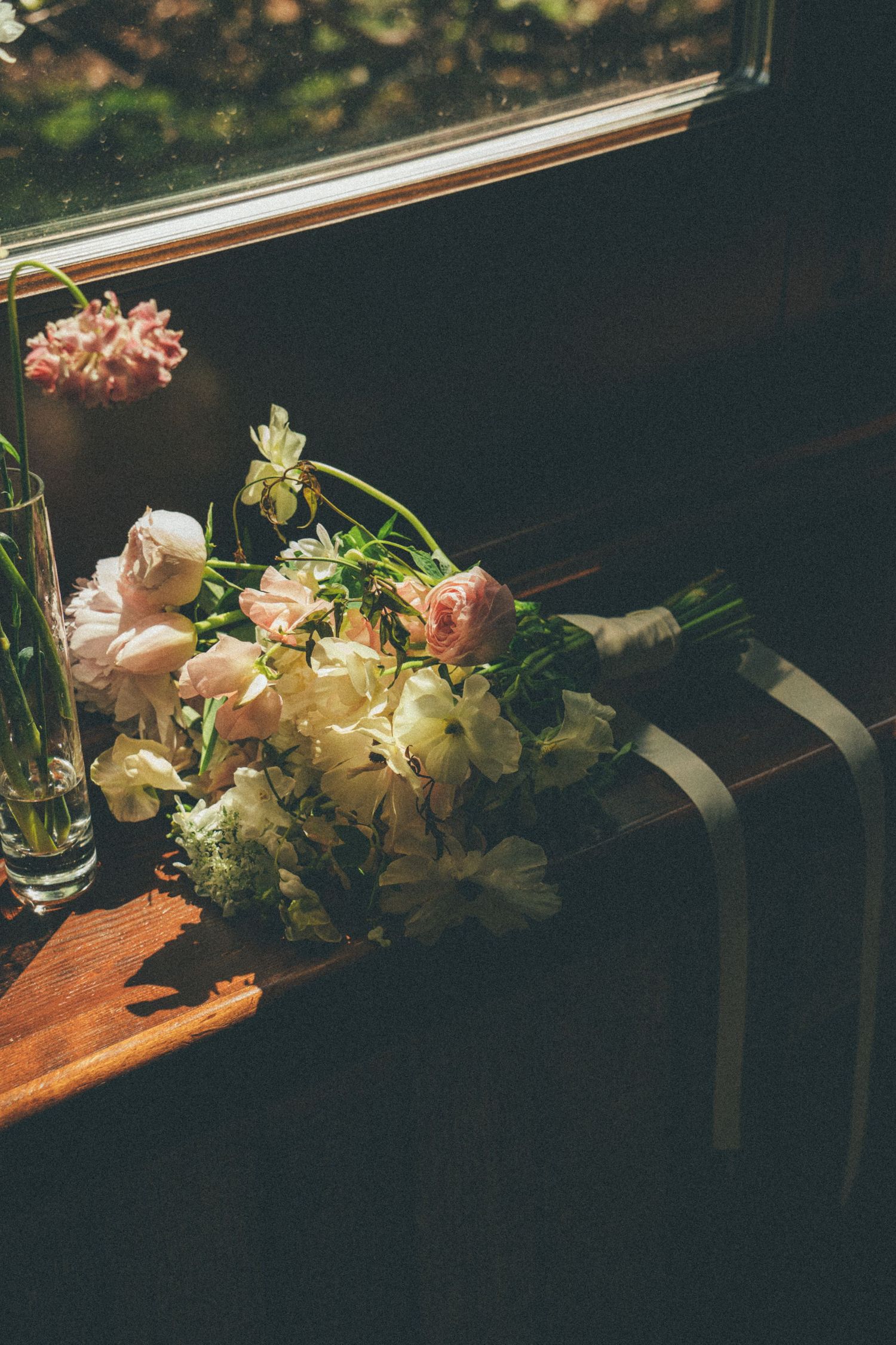 Bridal bouquet of pink and white roses resting on wooden bench near sunlit window.