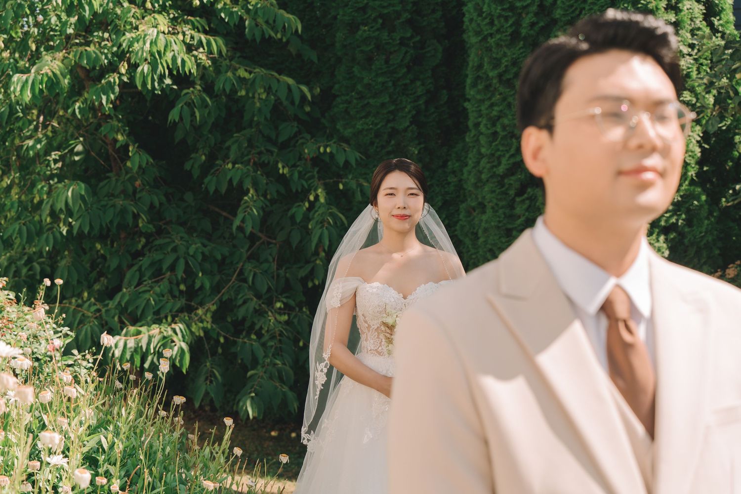 Bride in white gown and veil with groom in beige suit in garden.