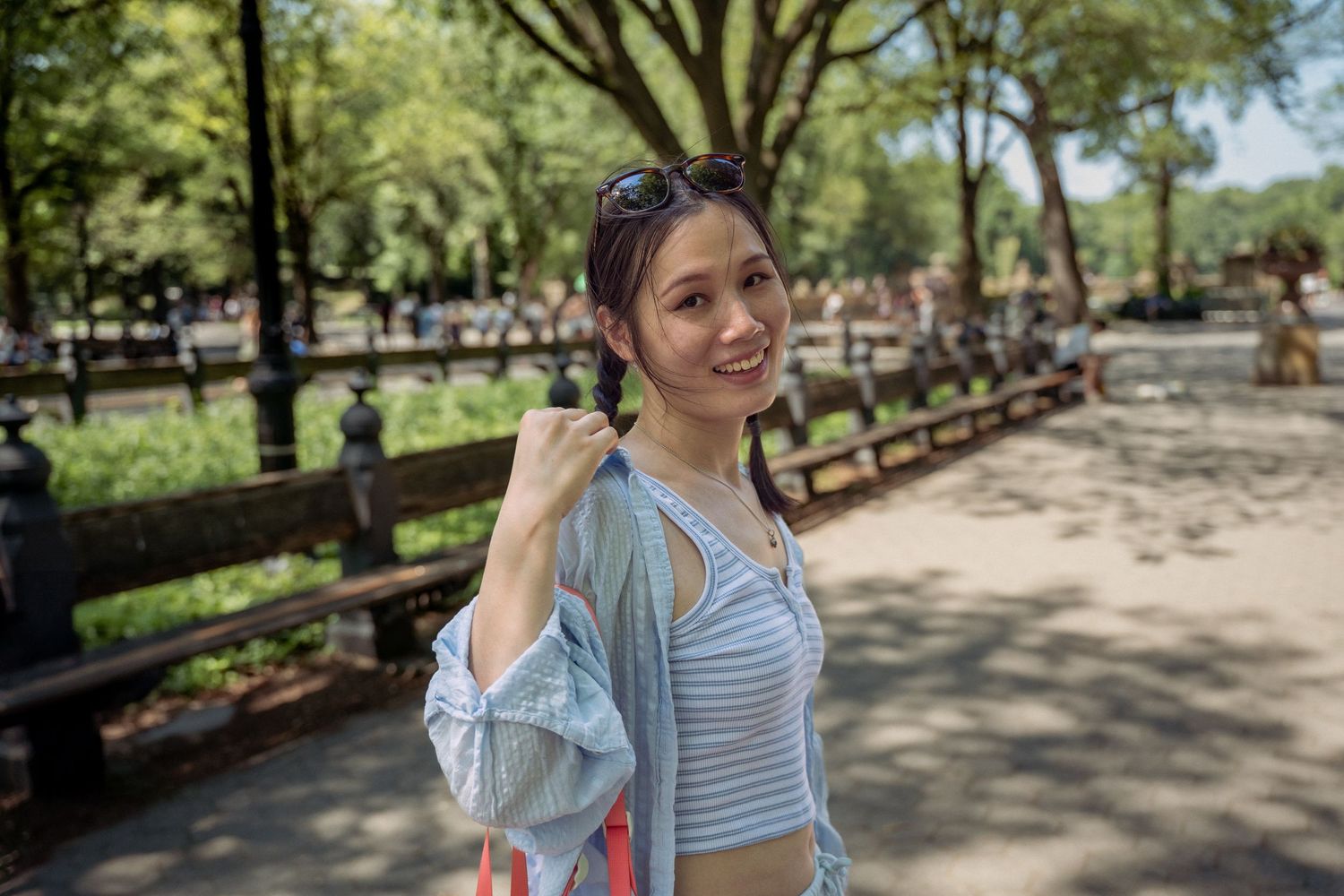 Smiling woman in blue striped crop top posing in a sunny park with green trees.