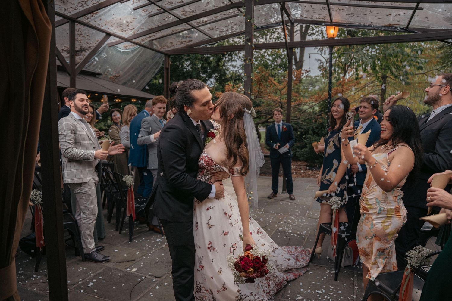 Bride and groom share a first kiss at their wedding ceremony under a glass pavilion.