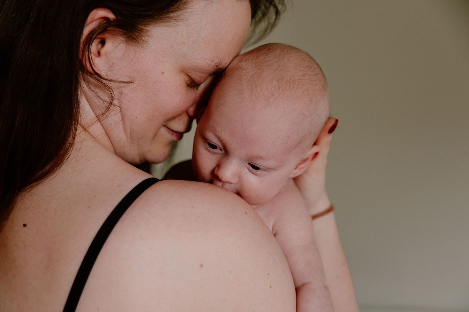 Mother tenderly holding and cuddling newborn baby against her shoulder indoors.
