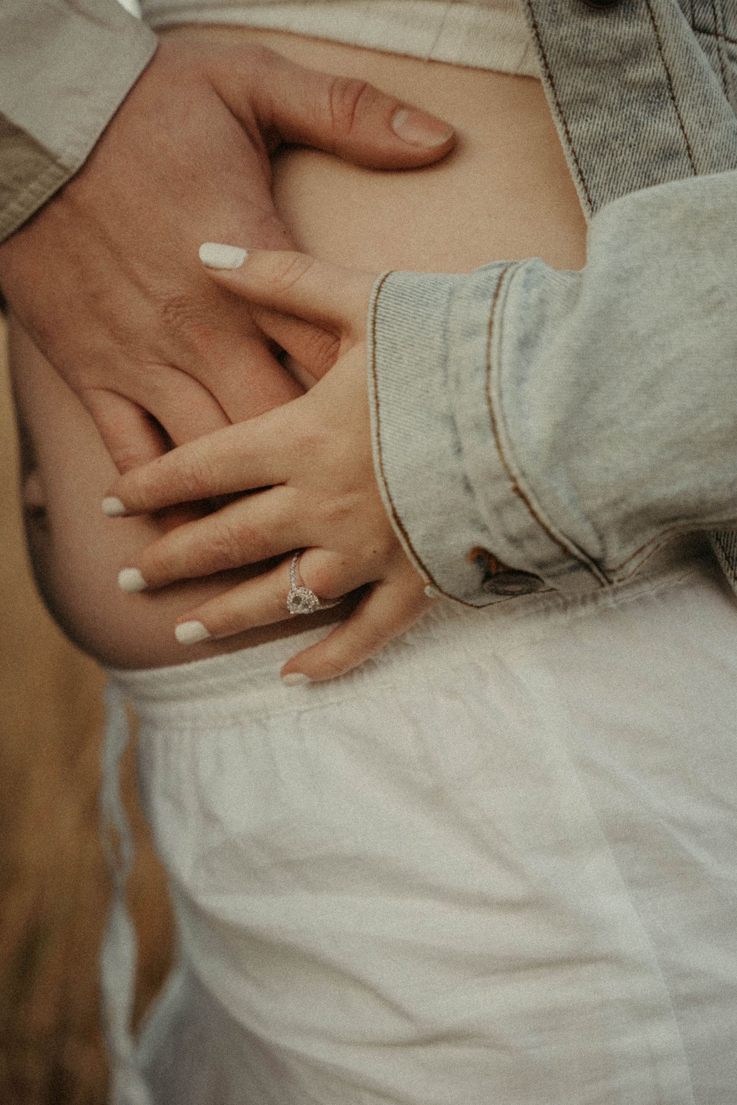 Close-up of couple's hands gently cradling a pregnant belly, woman wearing a diamond ring.