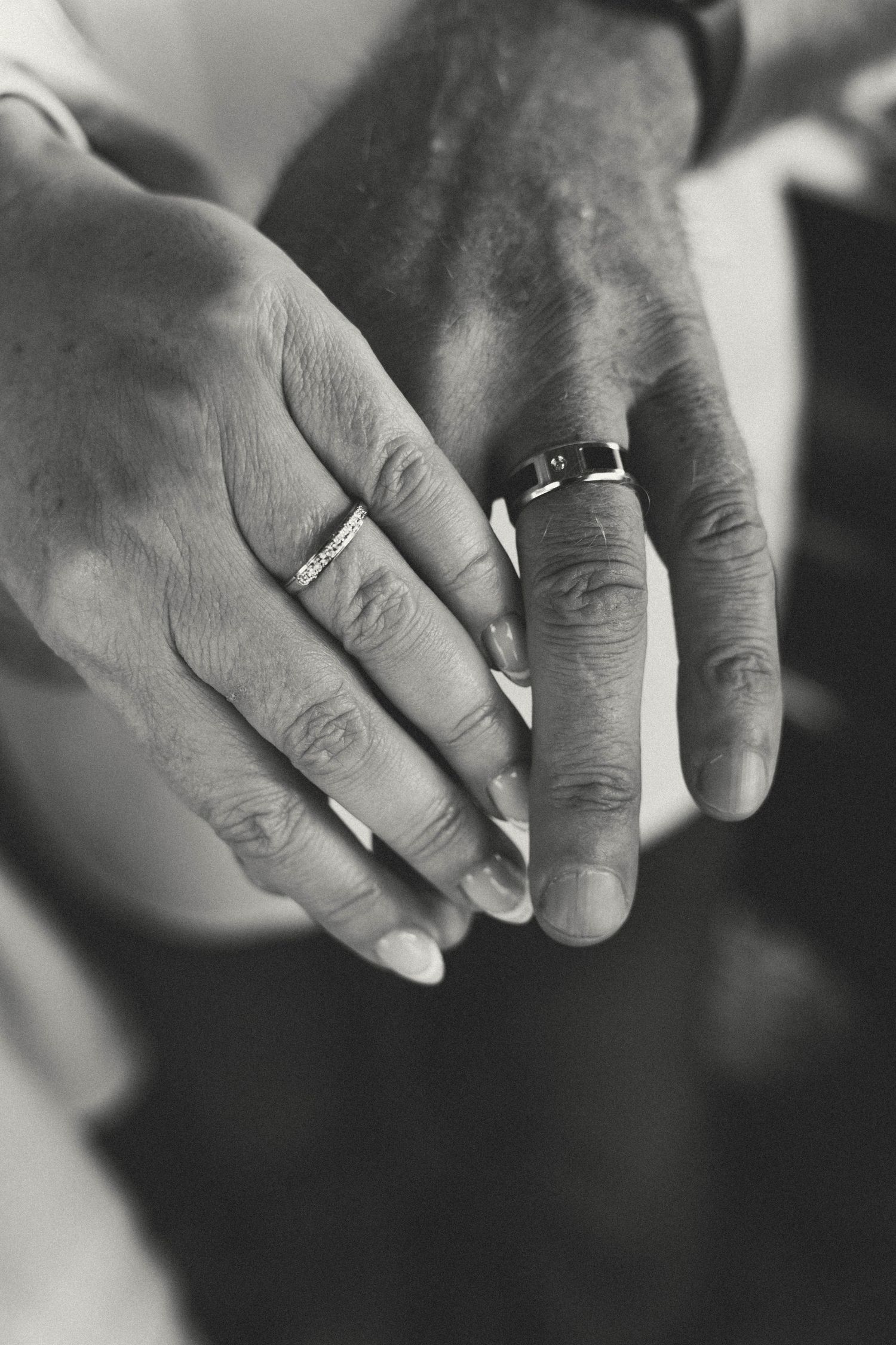 Close-up black and white photo of newlyweds hands displaying wedding rings after ceremony.