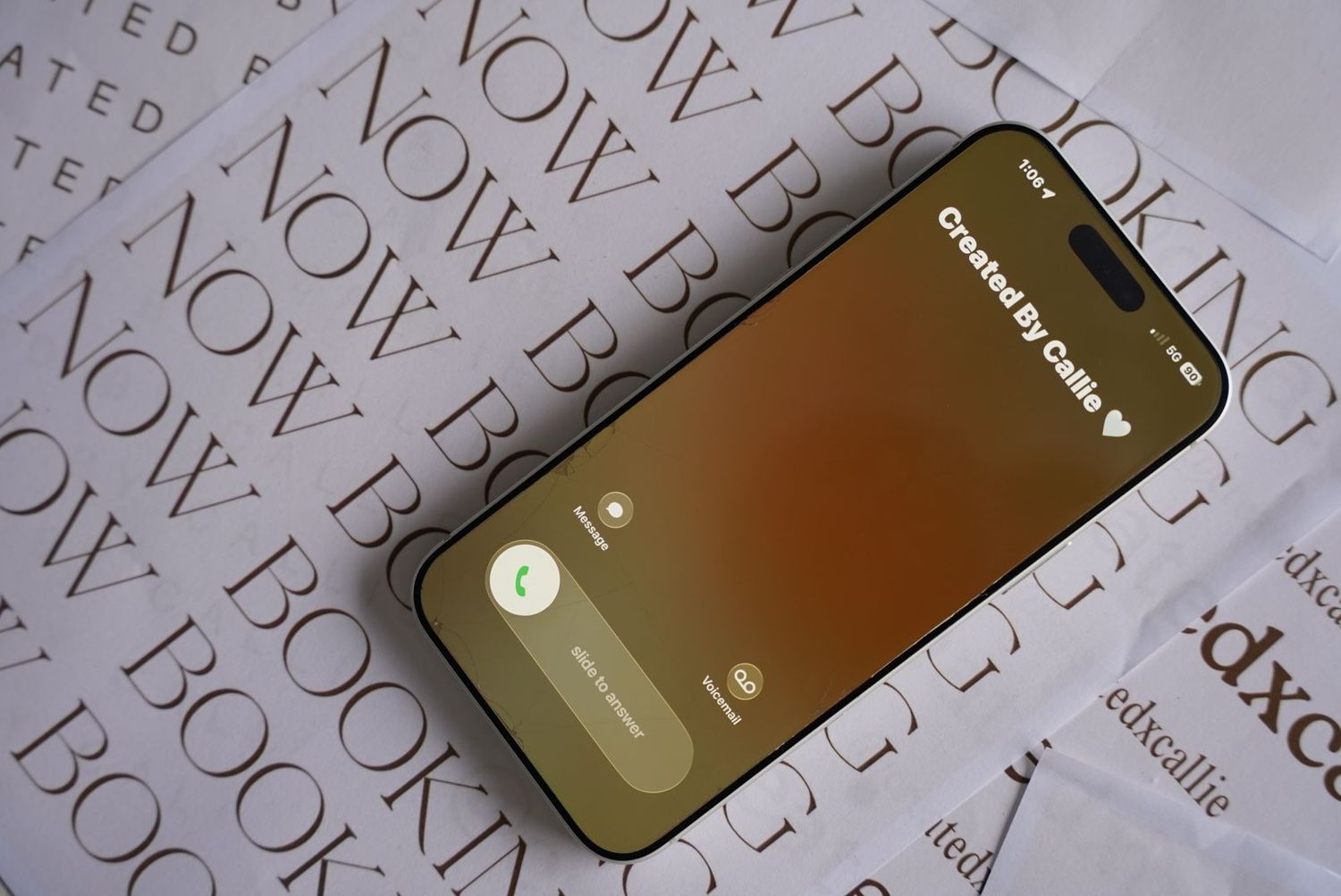 A smartphone displaying a call screen with 'Created By Callie' text, resting on a surface with booking-related text.