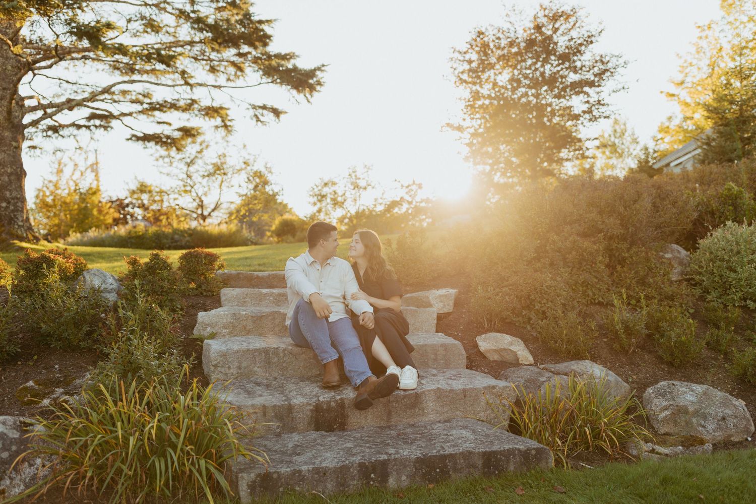 Couple sitting closely together on stone steps in a golden sunset garden setting.