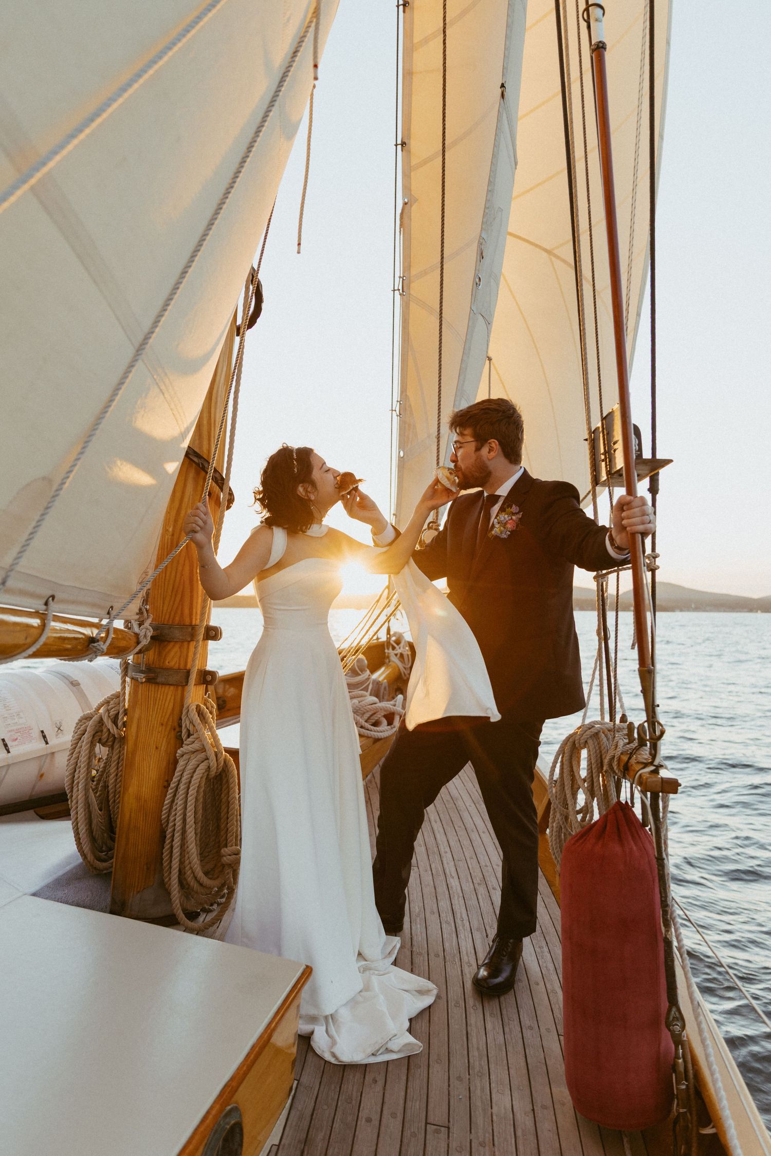Bride and groom toasting with champagne on a wooden sailboat deck at golden sunset.