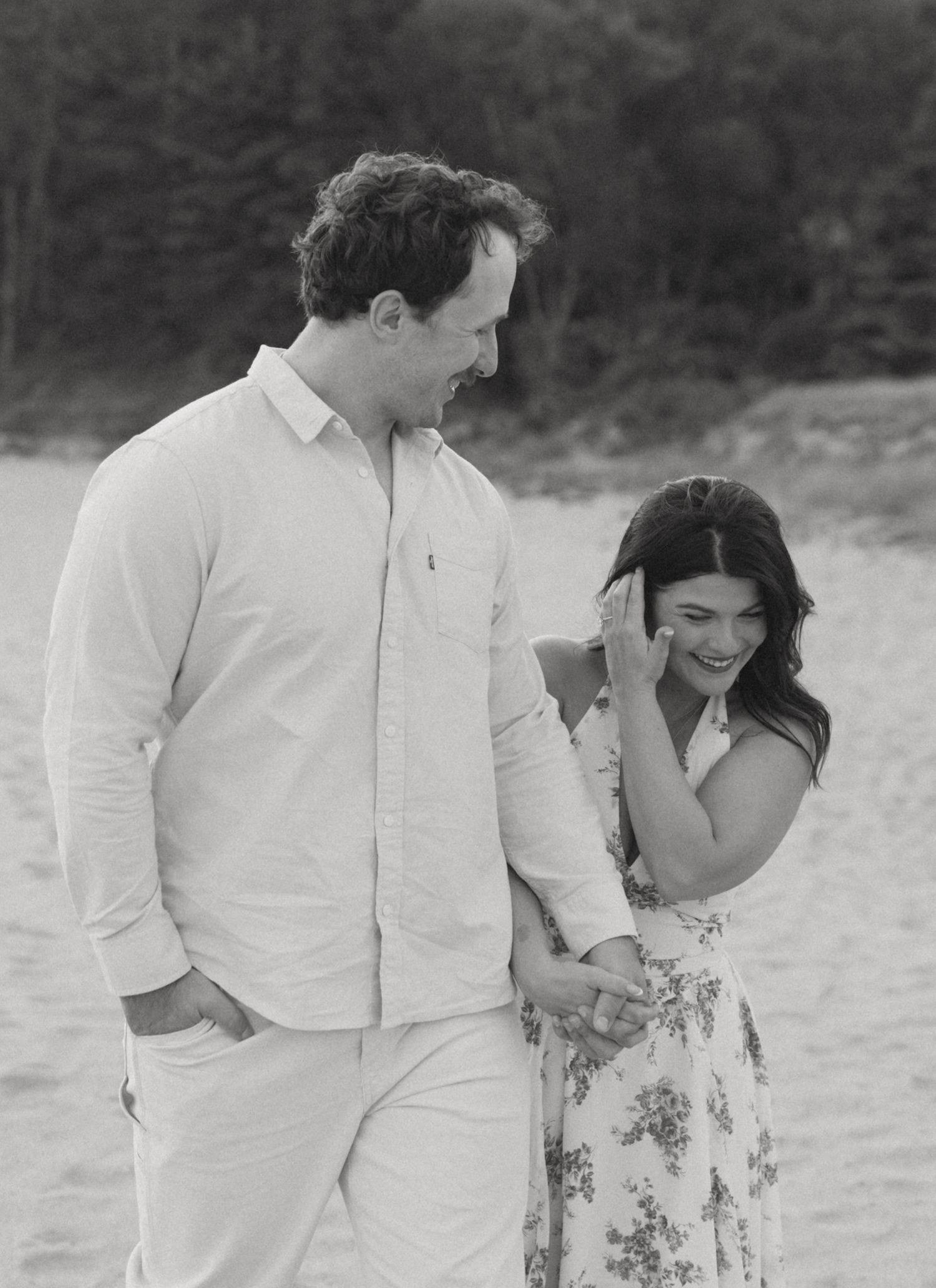 Black and white photo of smiling couple walking together on a sandy beach.