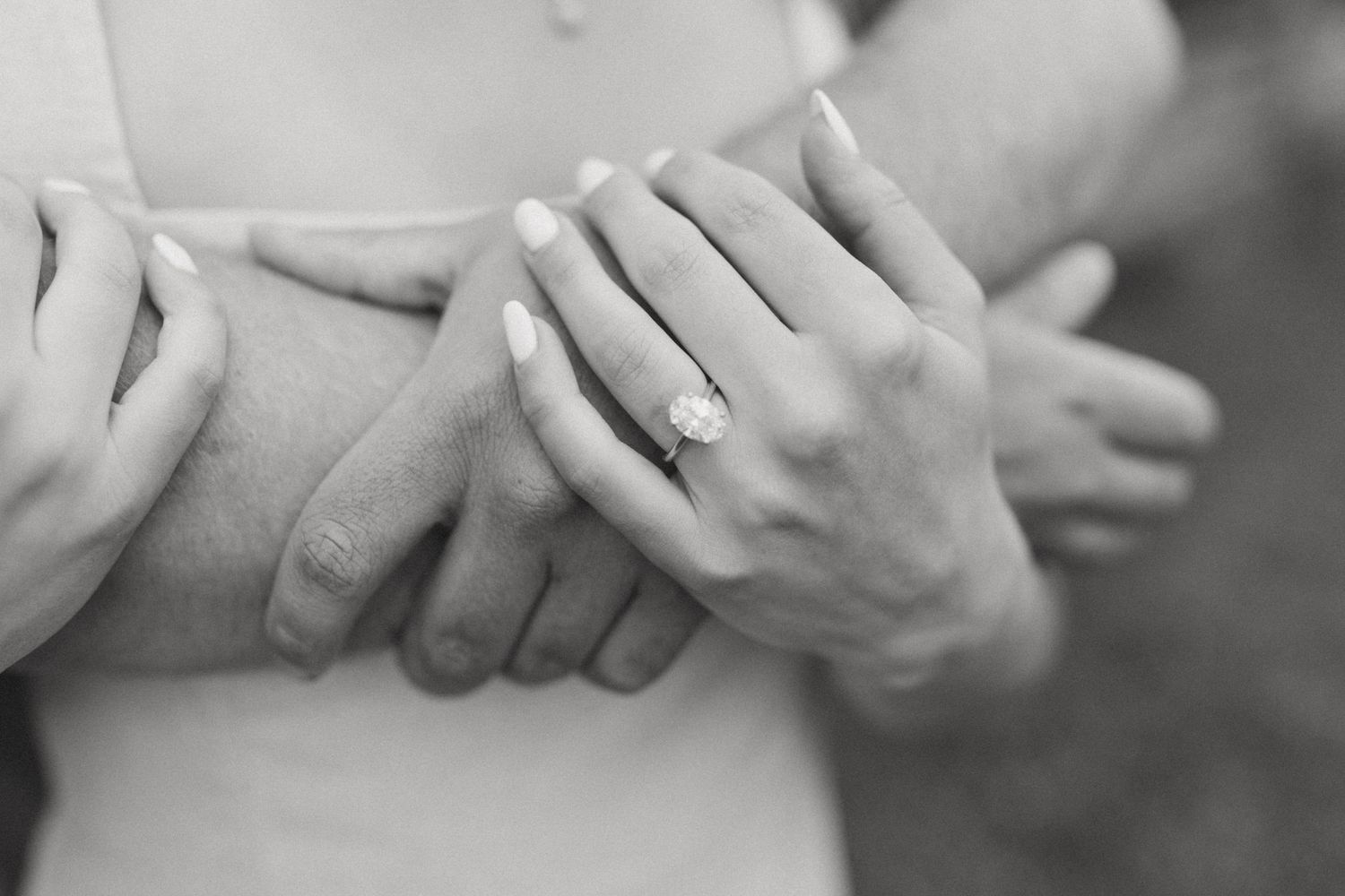 Close-up black and white photo of an engagement ring on a womans hand while embracing.