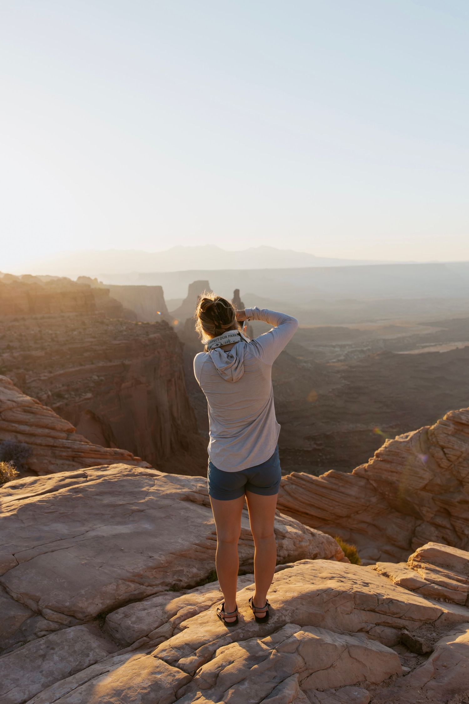 Woman photographs sweeping red rock canyon views from a clifftop overlook at golden hour in Utah.