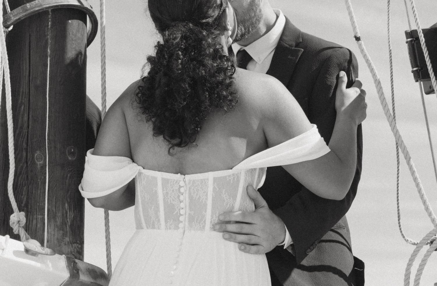 Bride and groom embracing on a sailboat deck in black and white wedding photo.