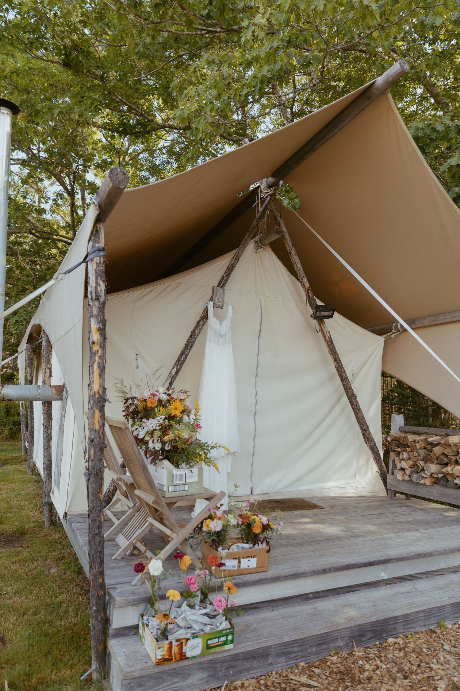 Decorated glamping tent with wooden porch, floral arrangements, and rustic wood details for a wedding.