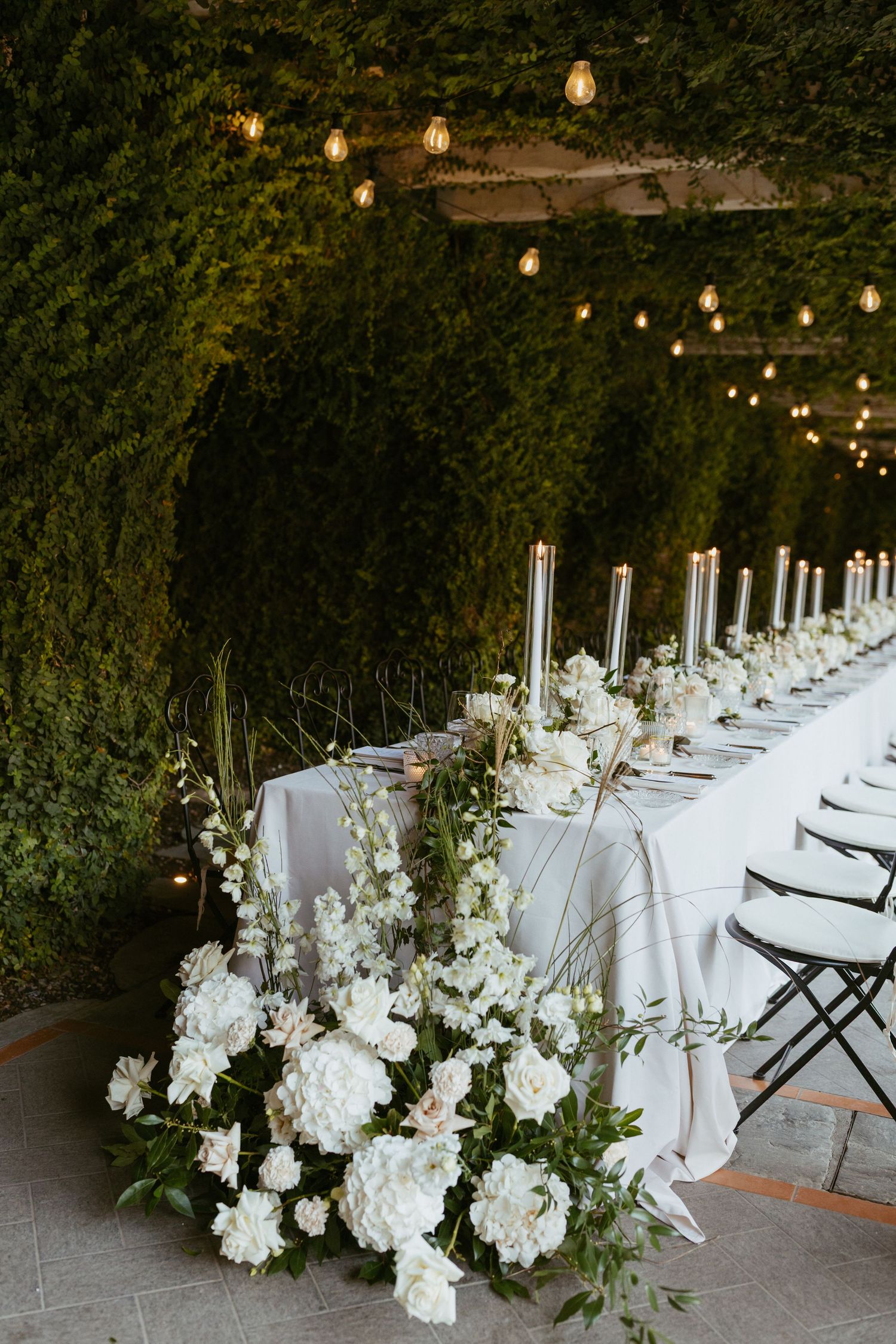 Elegant outdoor wedding reception table with white floral arrangements and string lights.