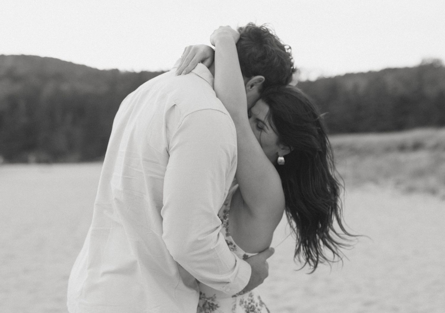 Black and white photo of a couple sharing an intimate embrace on a beach.
