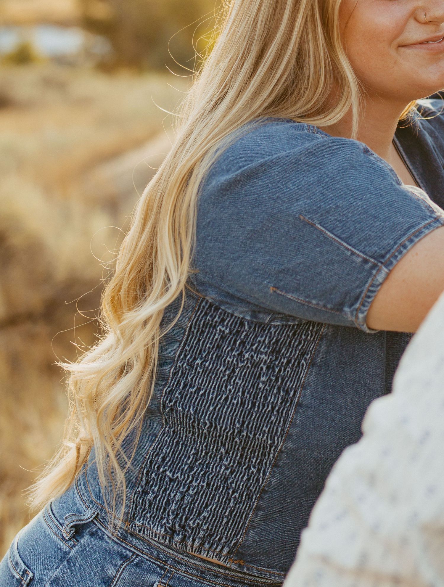 Close-up of blonde woman in smocked denim with long wavy hair in golden outdoor natural light.
