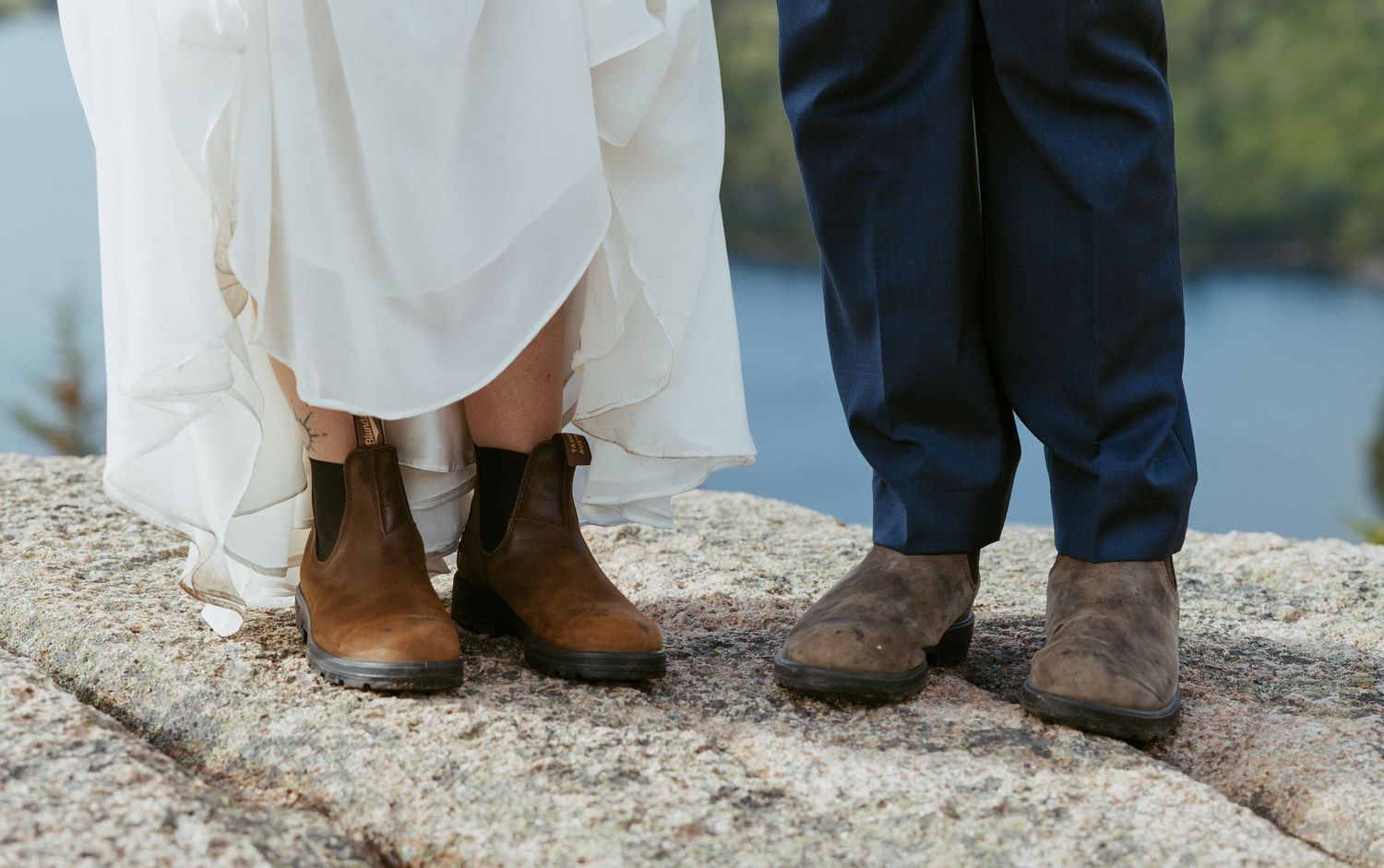 Bride in white dress and groom in navy suit both wearing matching brown leather boots on rocky outdoor wedding venue.
