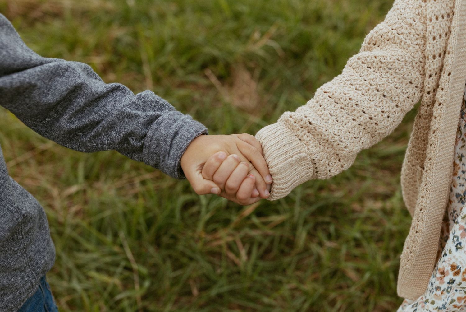 Two children holding hands in a grassy field, wearing cozy sweaters, symbolizing friendship and connection.