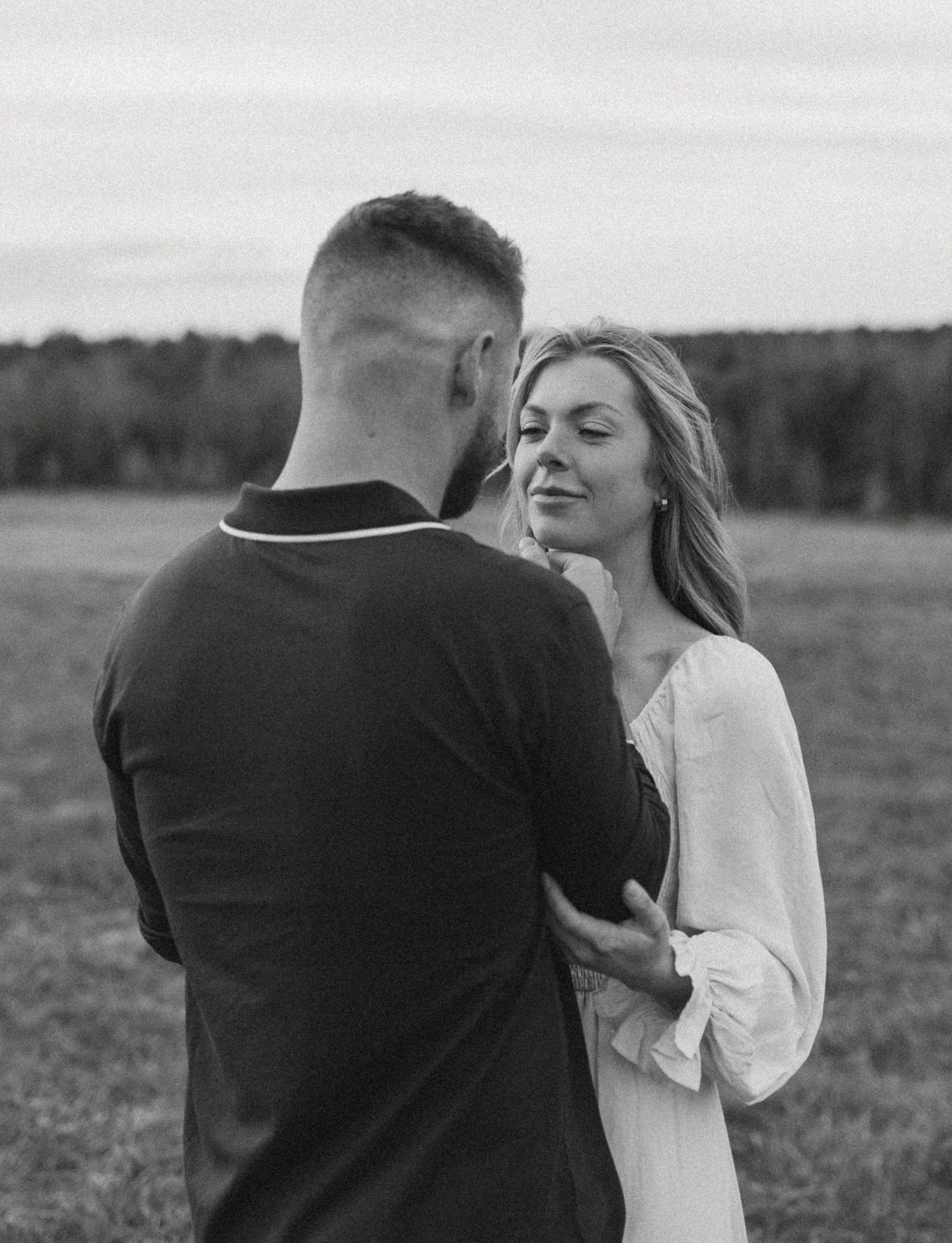 Black and white photo of a couple embracing in an open field at dusk.