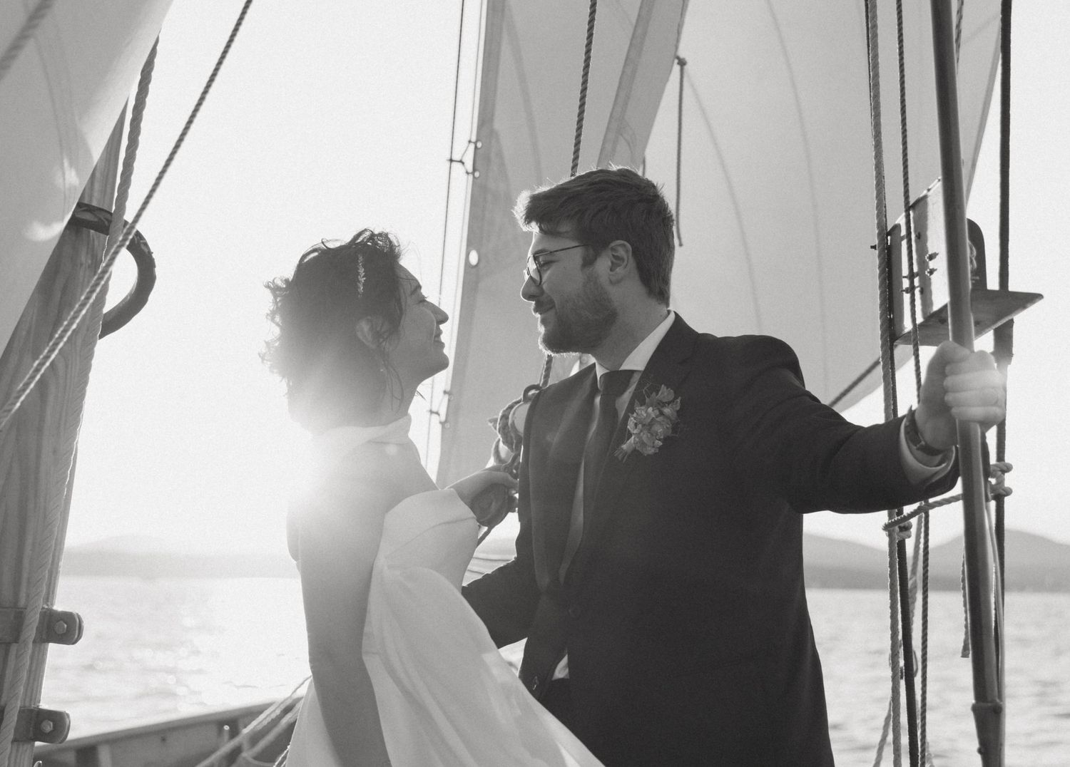 Black and white photo of newlyweds sharing an intimate moment aboard a sailing vessel at sea.