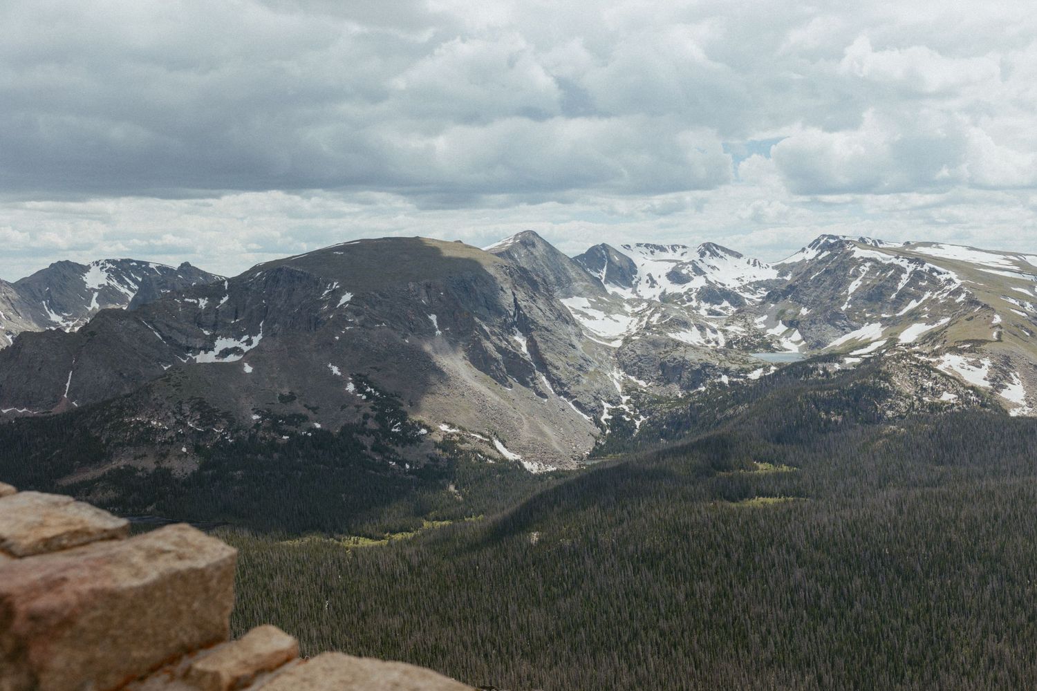 Snow-capped Rocky Mountain peaks with evergreen forests under cloudy skies in Colorado.