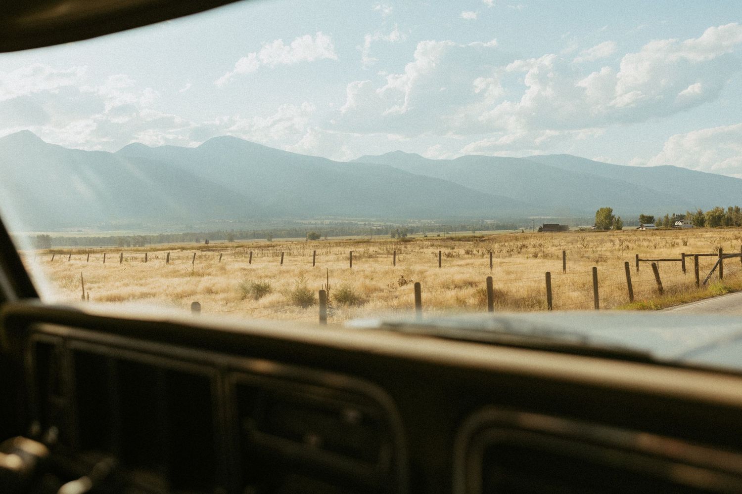 Scenic view of open Montana mountain fields and fence lines through the windshield of a vintage classic truck.
