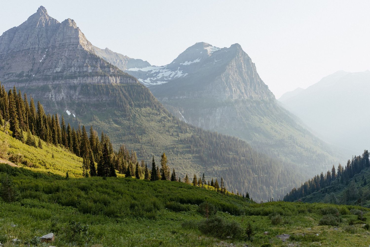 Majestic mountain valley landscape with lush green meadows and misty peaks in the background.