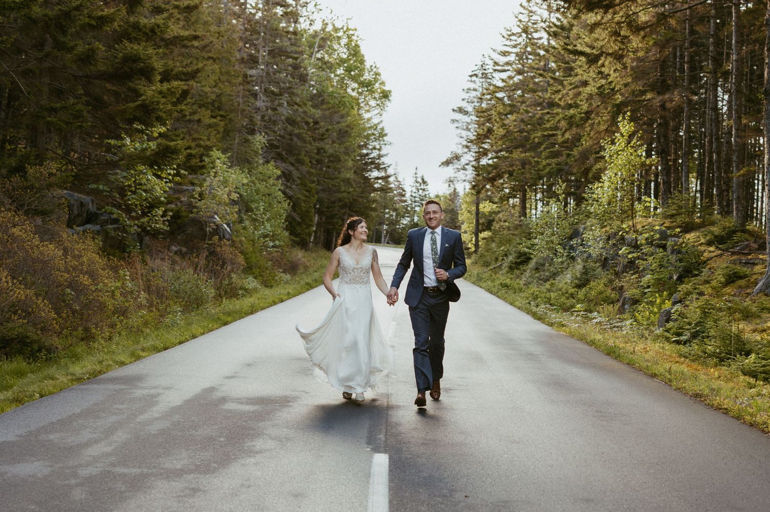 Bride and groom walking hand in hand down a scenic forest road on their wedding day.