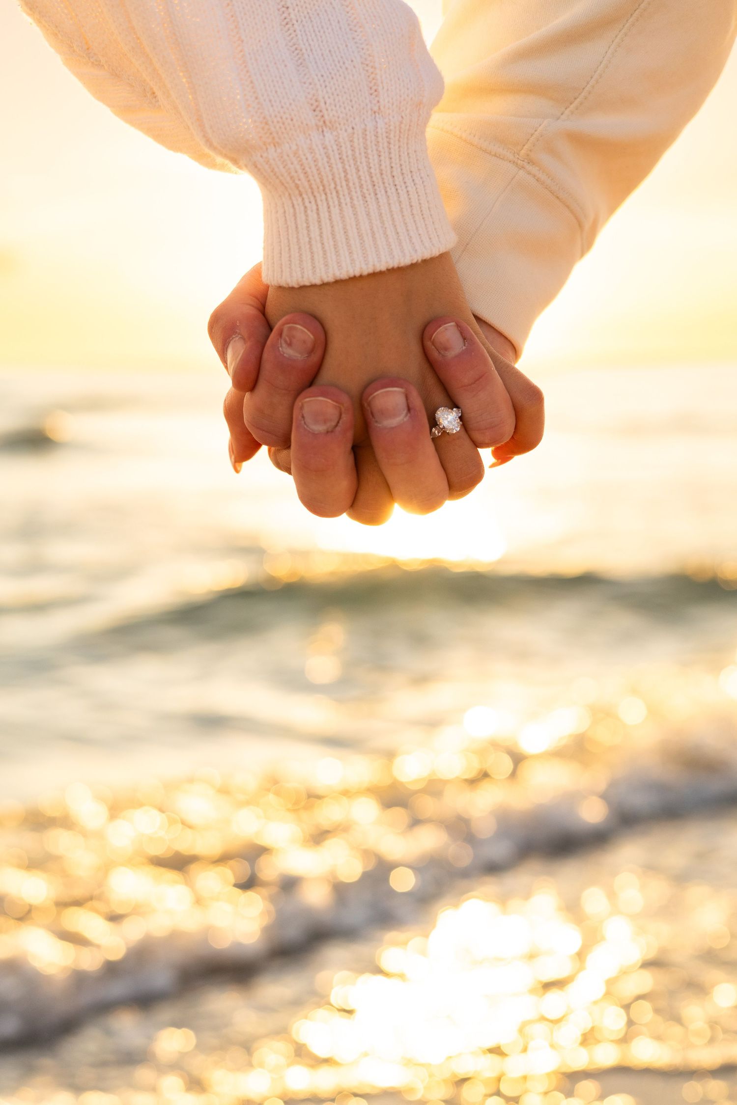 Couple holding hands on beach at sunset with diamond engagement ring visible Sarasota Florida engagement photographer