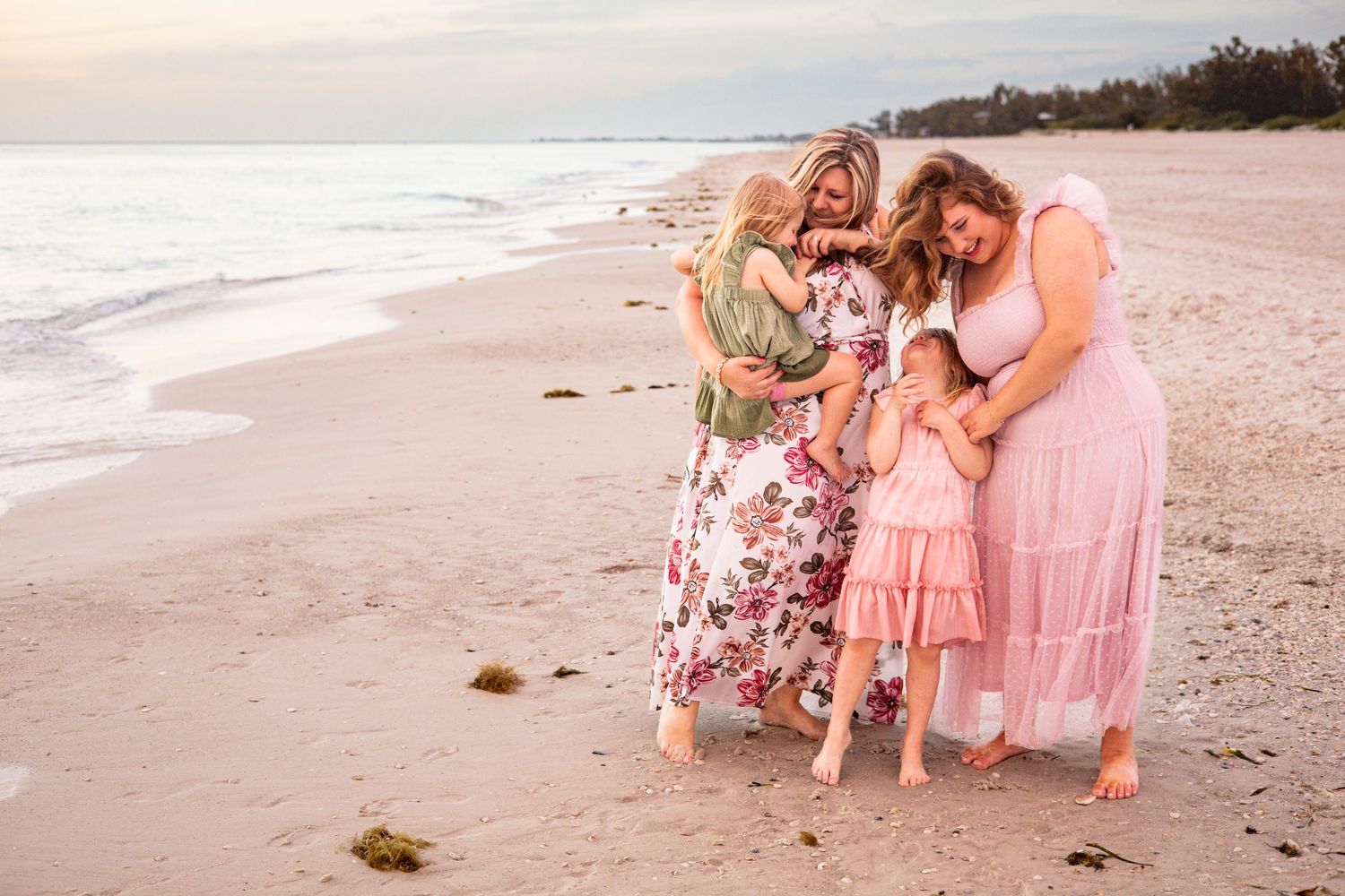 Two women and two children in pink dresses embrace on a sandy beach at sunset In Sarasota Florida