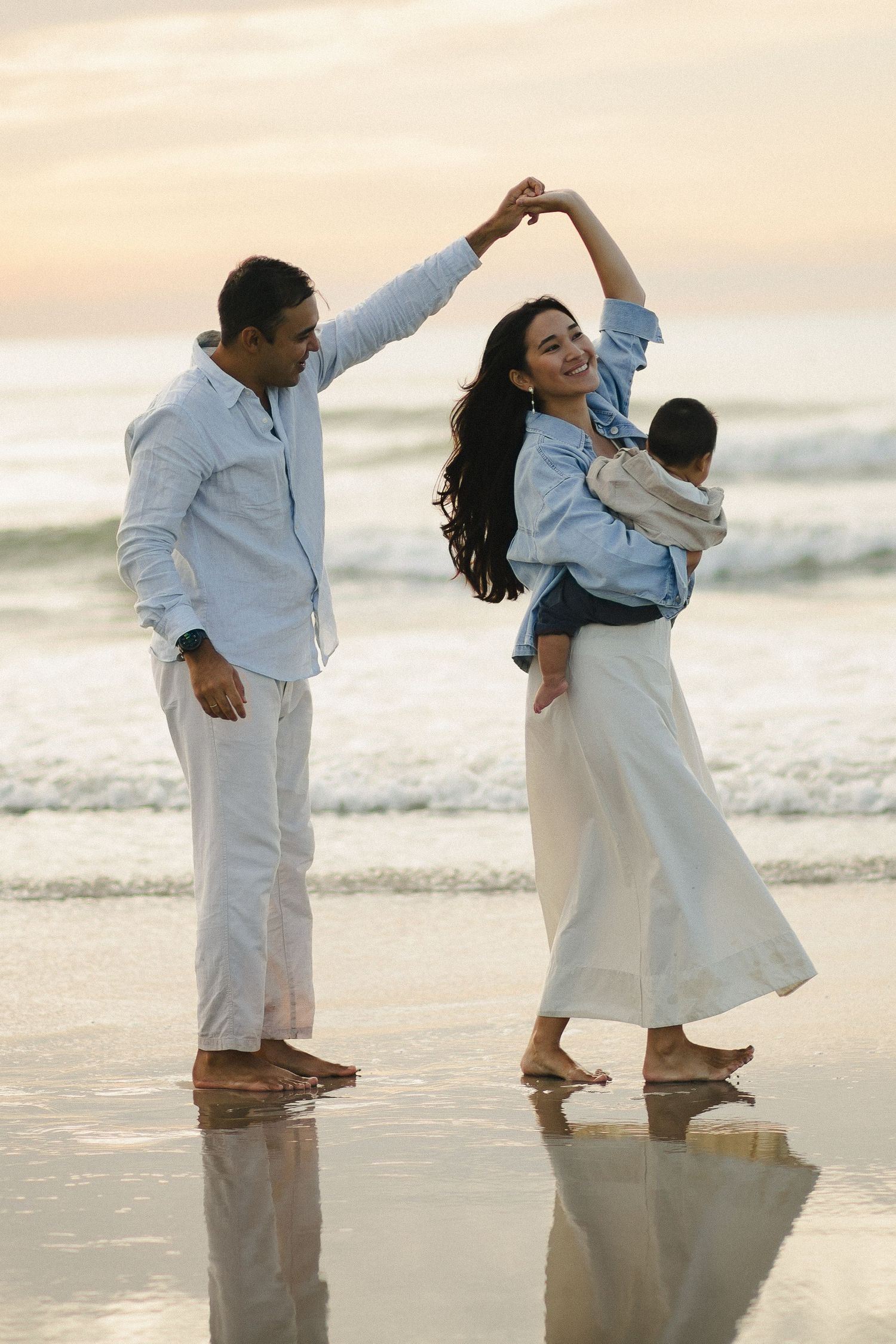 Parents dancing together while holding their baby at the beach