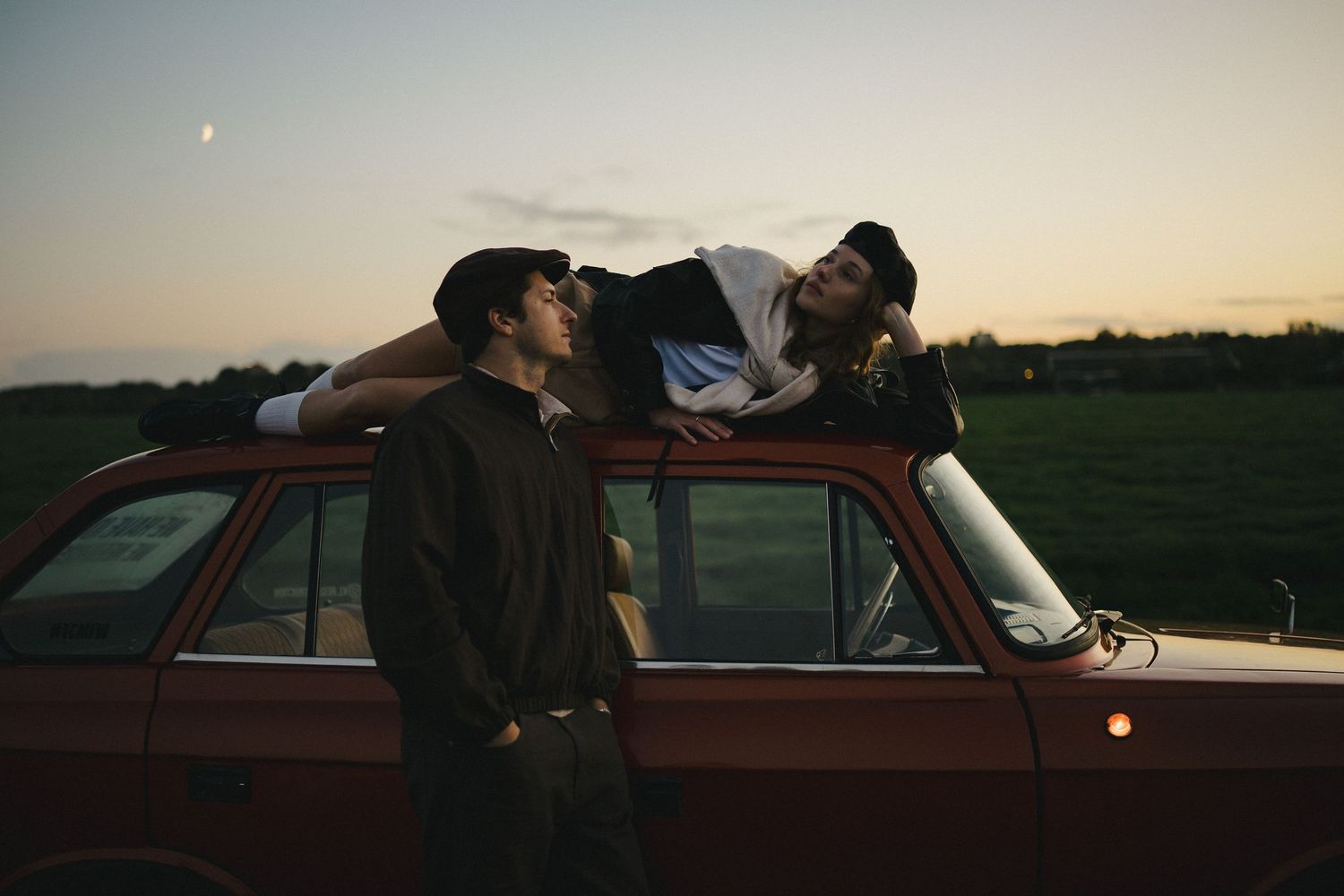 Couple sharing a playful moment by a vintage car at sunset