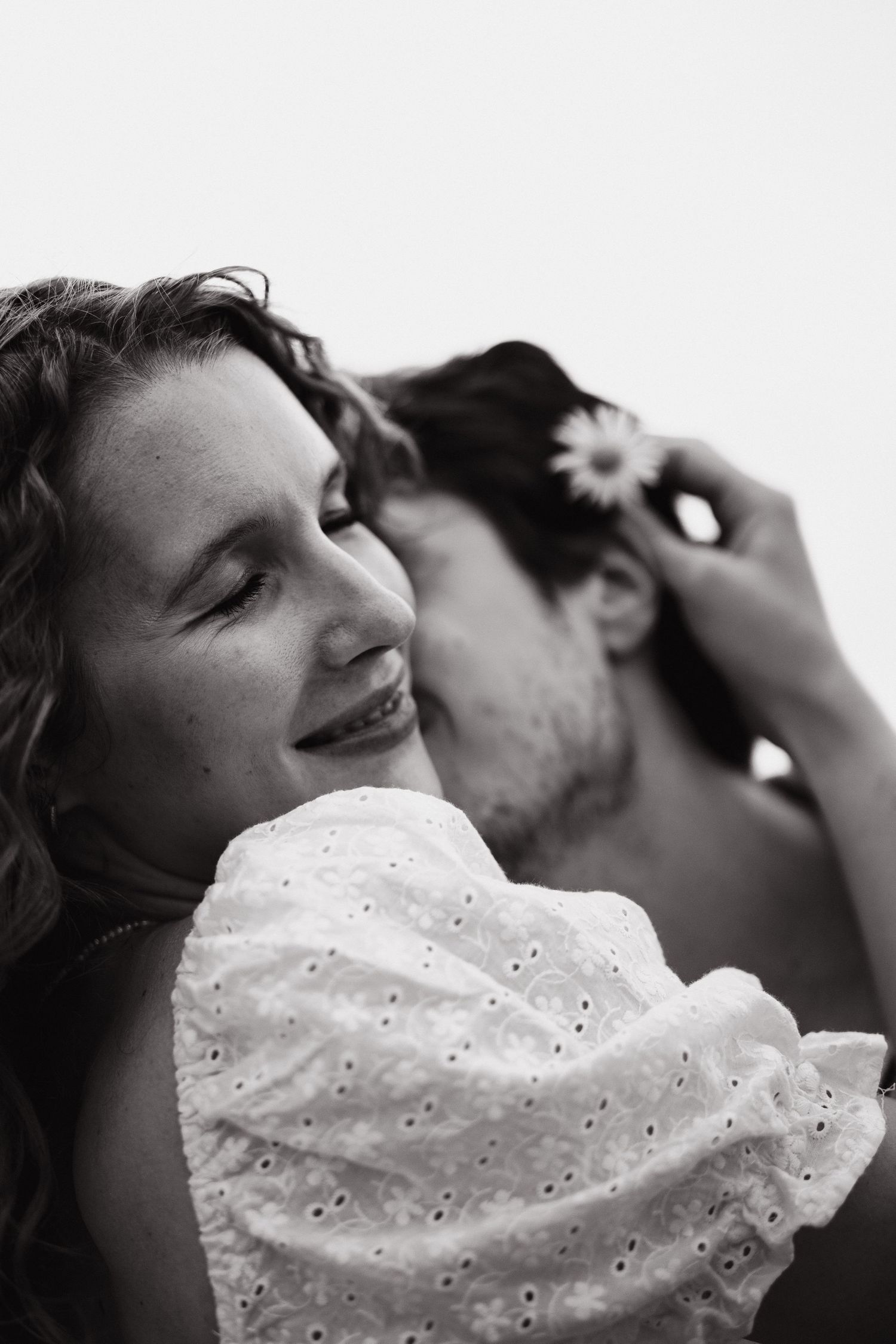 Black and white photo of a woman smiling as her partner kisses her cheek