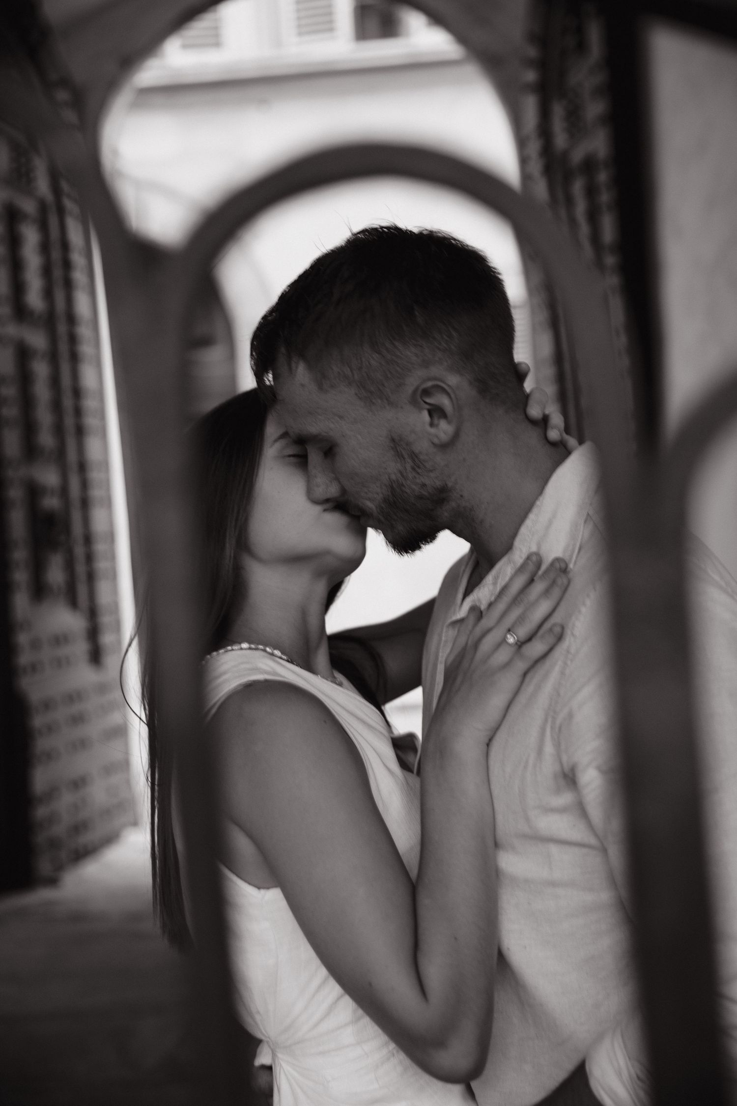 Black and white photo of a couple kissing beneath an archway