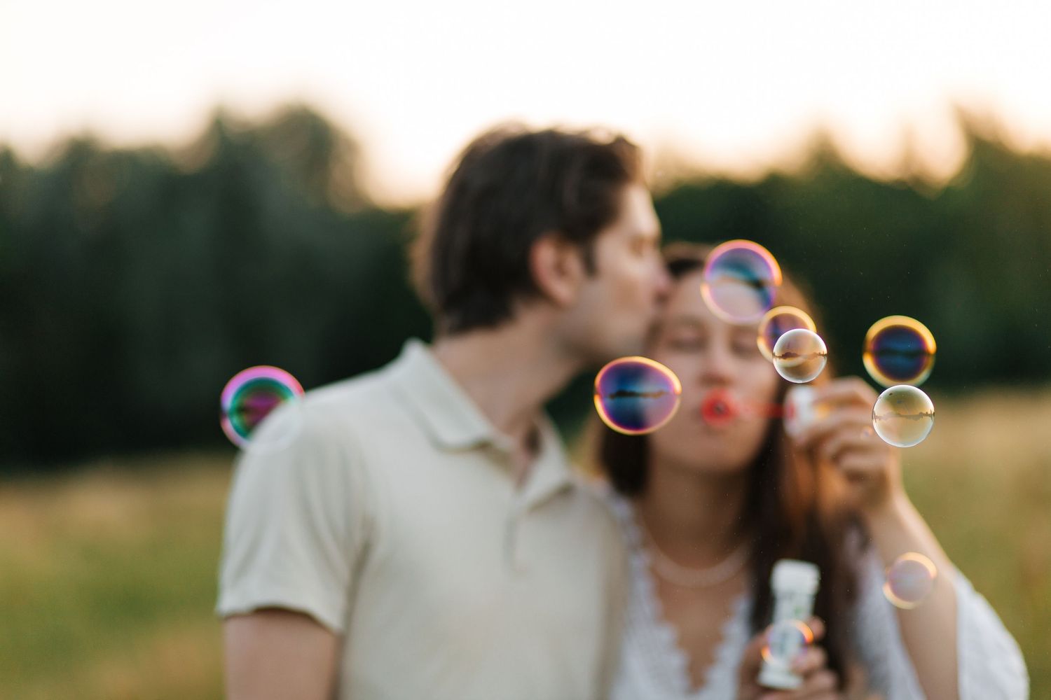 Couple laughing together as they blow bubbles in a sunlit field
