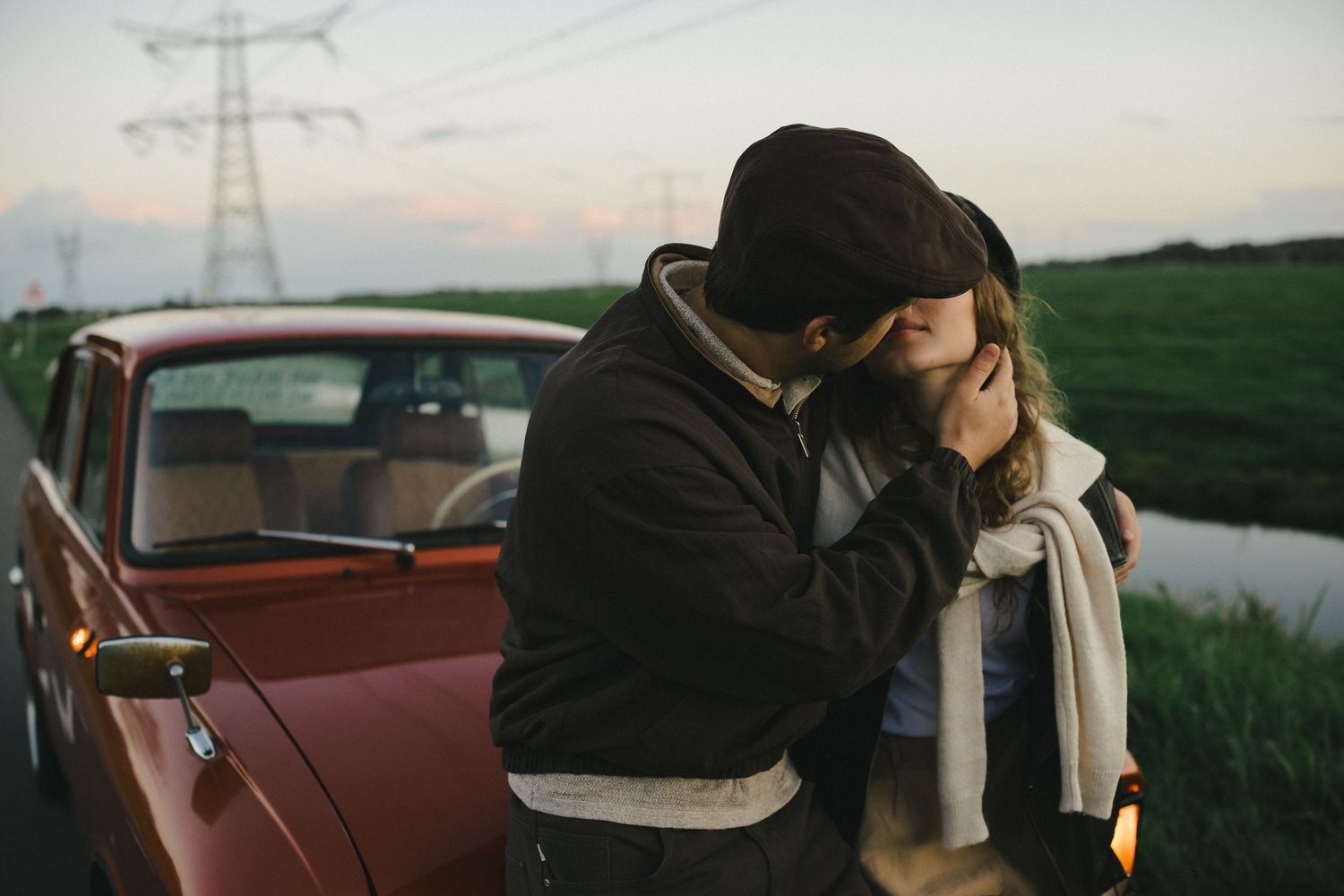 Couple kissing beside a vintage car in the countryside