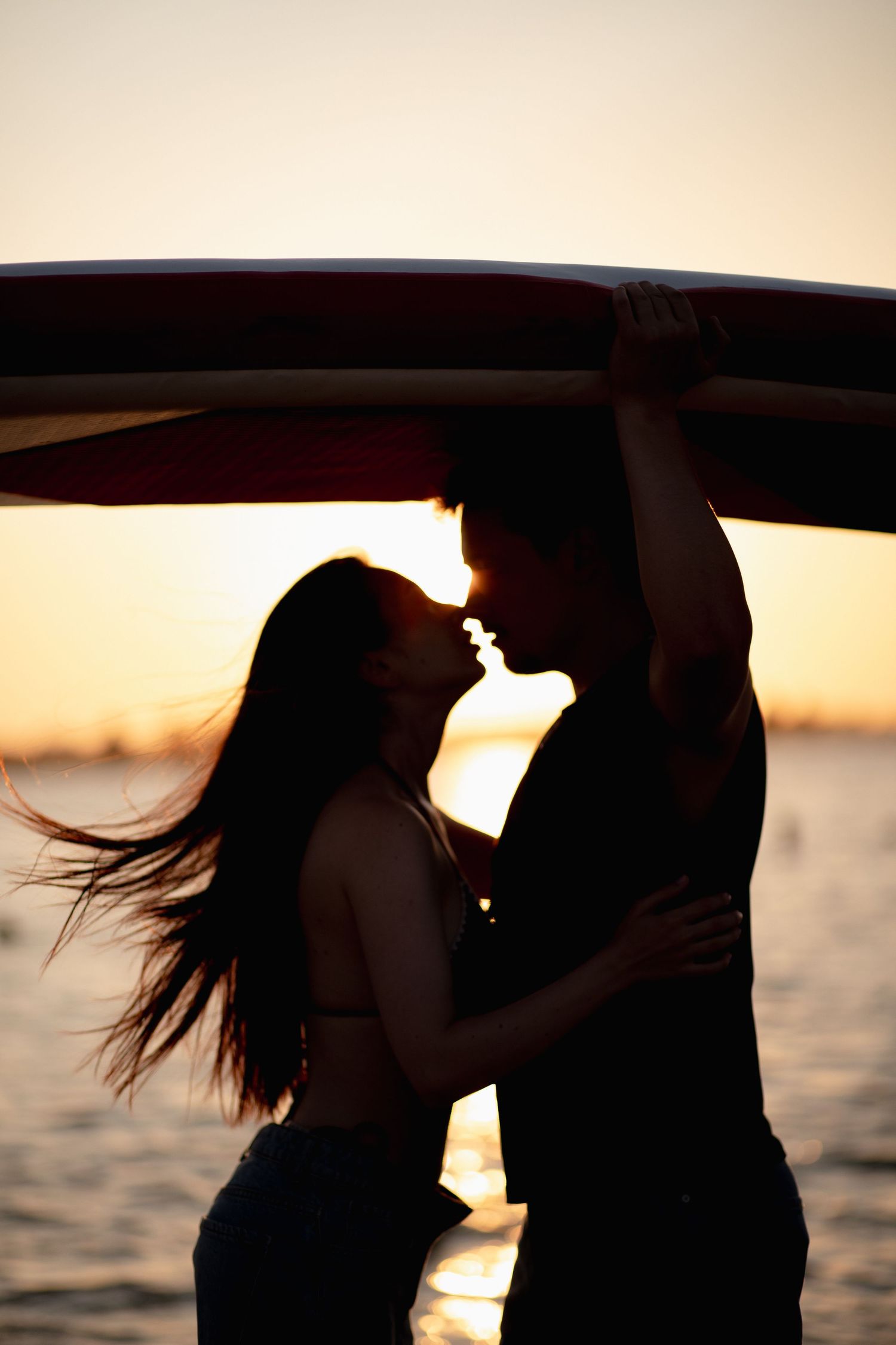 Silhouette of a couple embracing beneath a paddleboard at sunset
