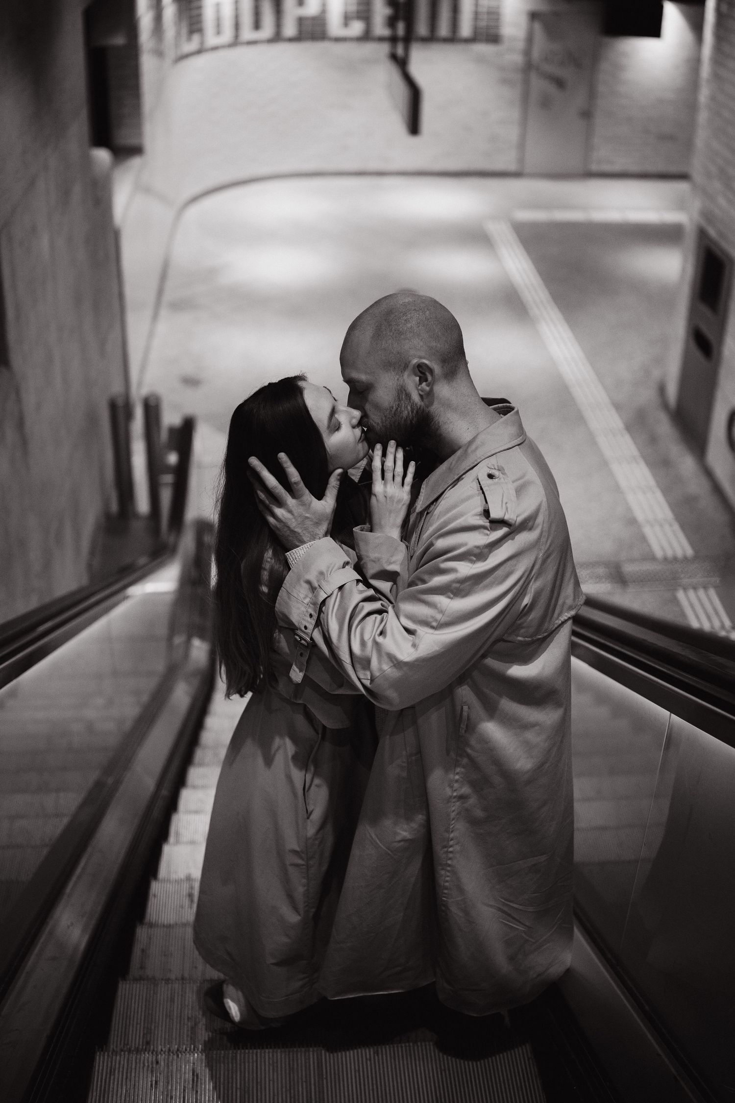 Black and white photo of a couple embracing on an escalator