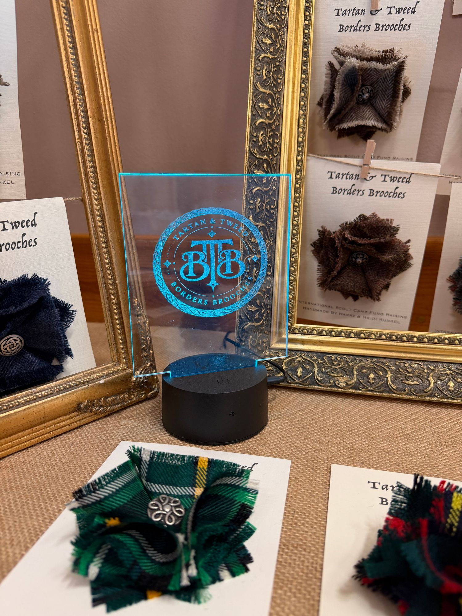 Gold-framed displays showing fabric samples with a glowing blue LED light centerpiece on a beige surface.