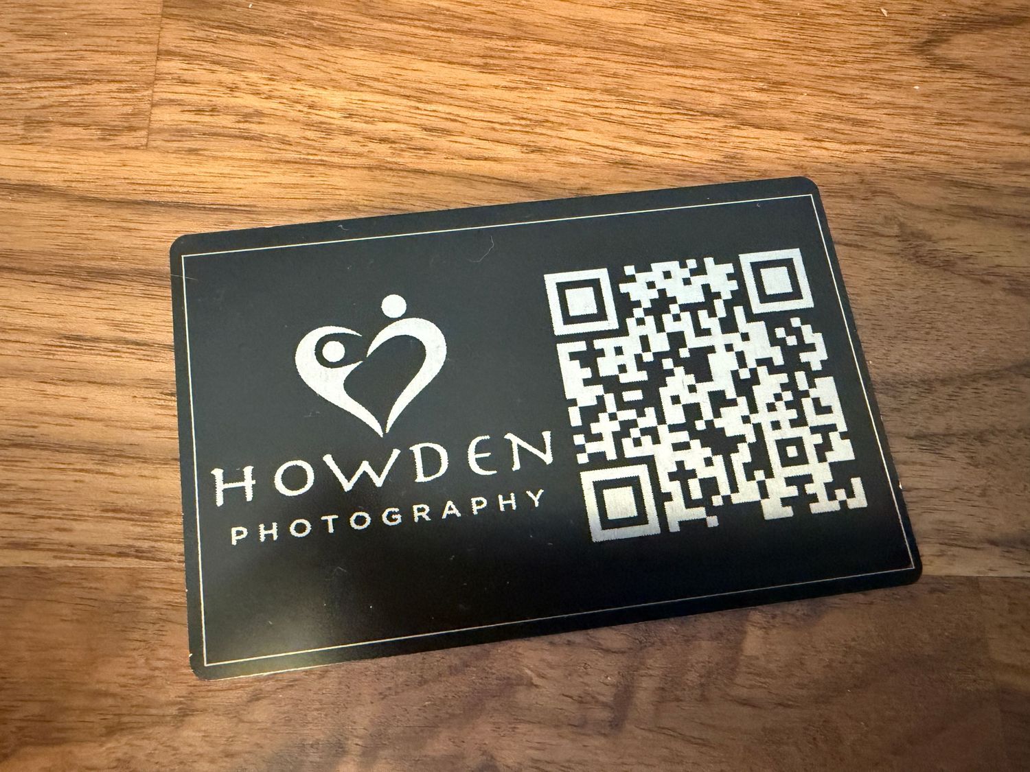 A series of black business cards with QR codes and photography branding laid out on a wooden surface.