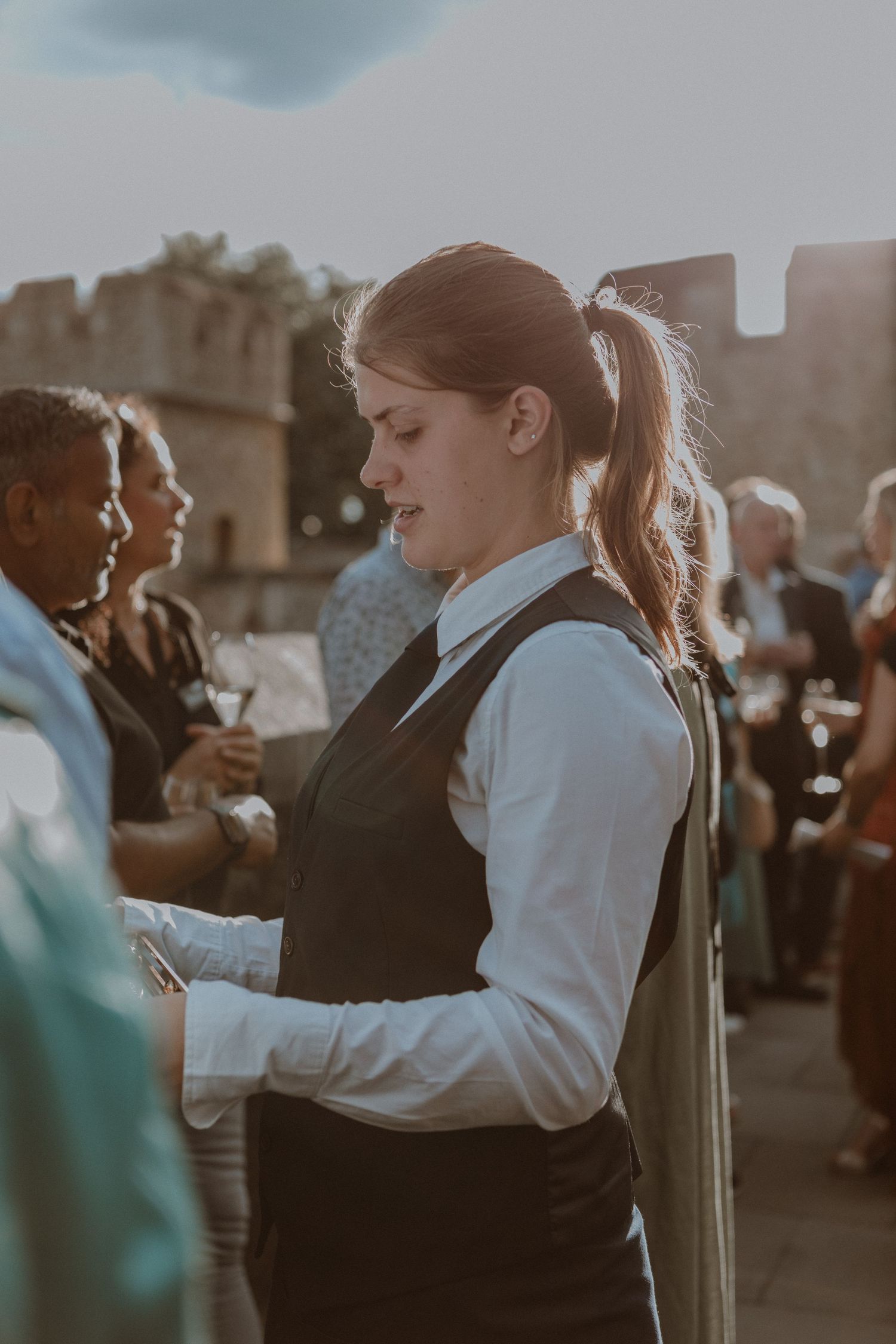 A server in professional attire taking orders during an outdoor catering event.