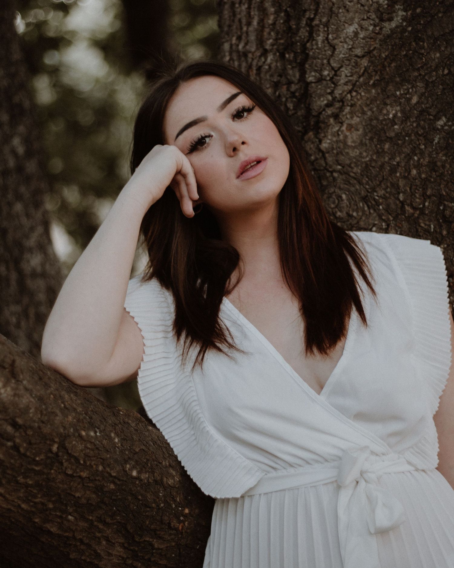 A dreamy portrait against a tree in a white pleated dress.